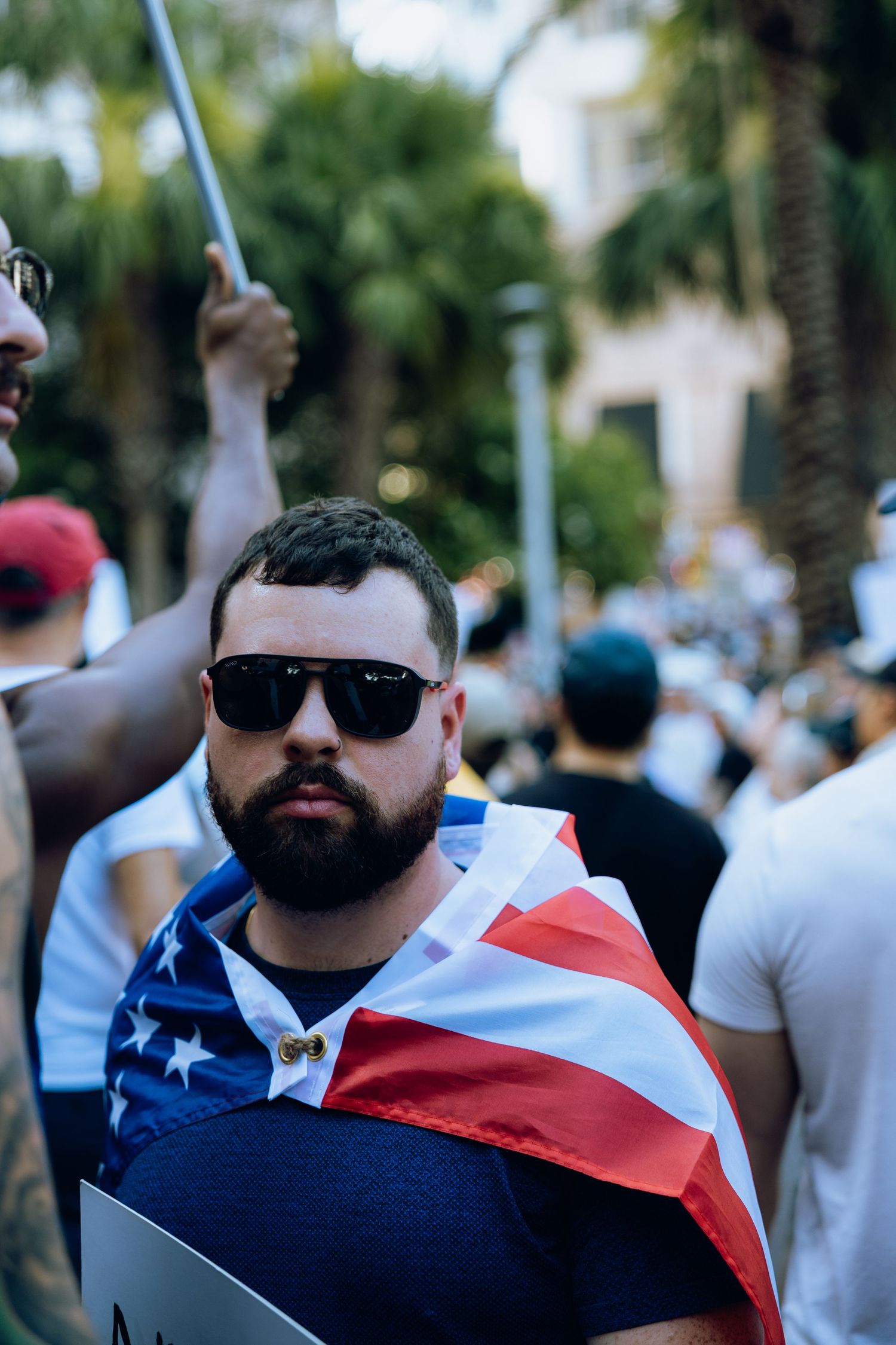 People in a crowd holding American flags and signs during a daytime protest or rally.