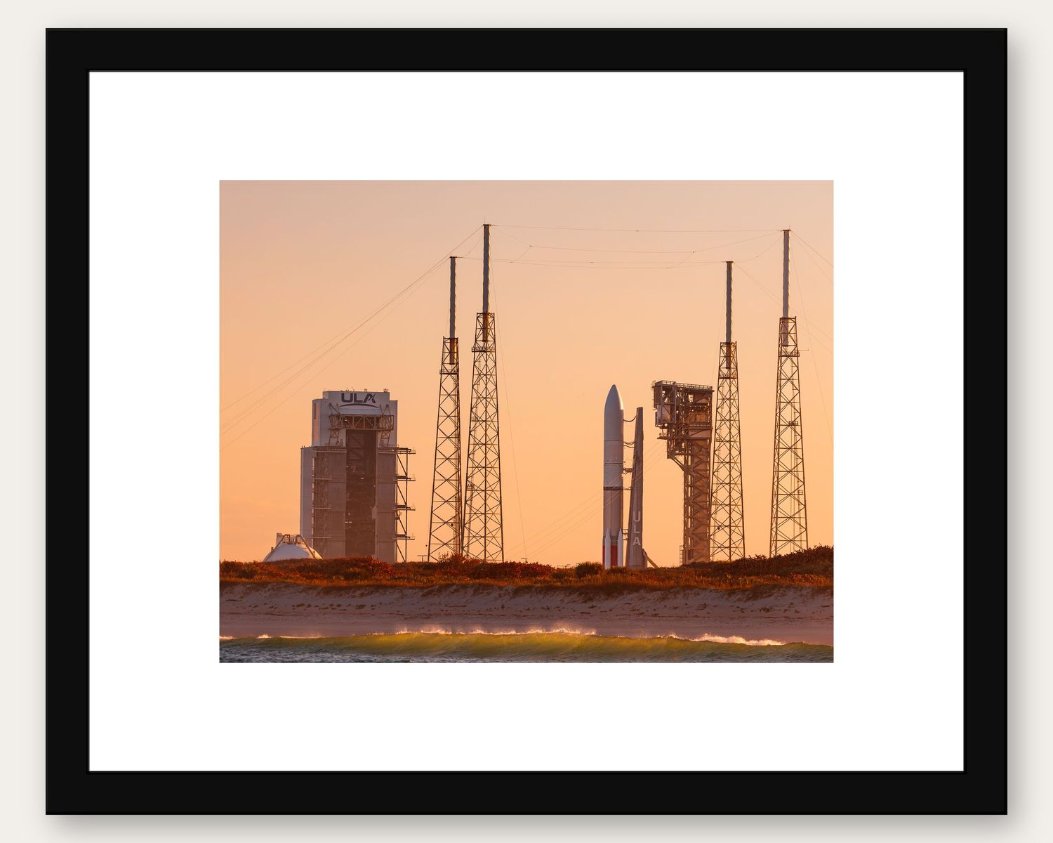 Framed photo of rocket launch pads at sunset with orange sky at Cape Canaveral space center.