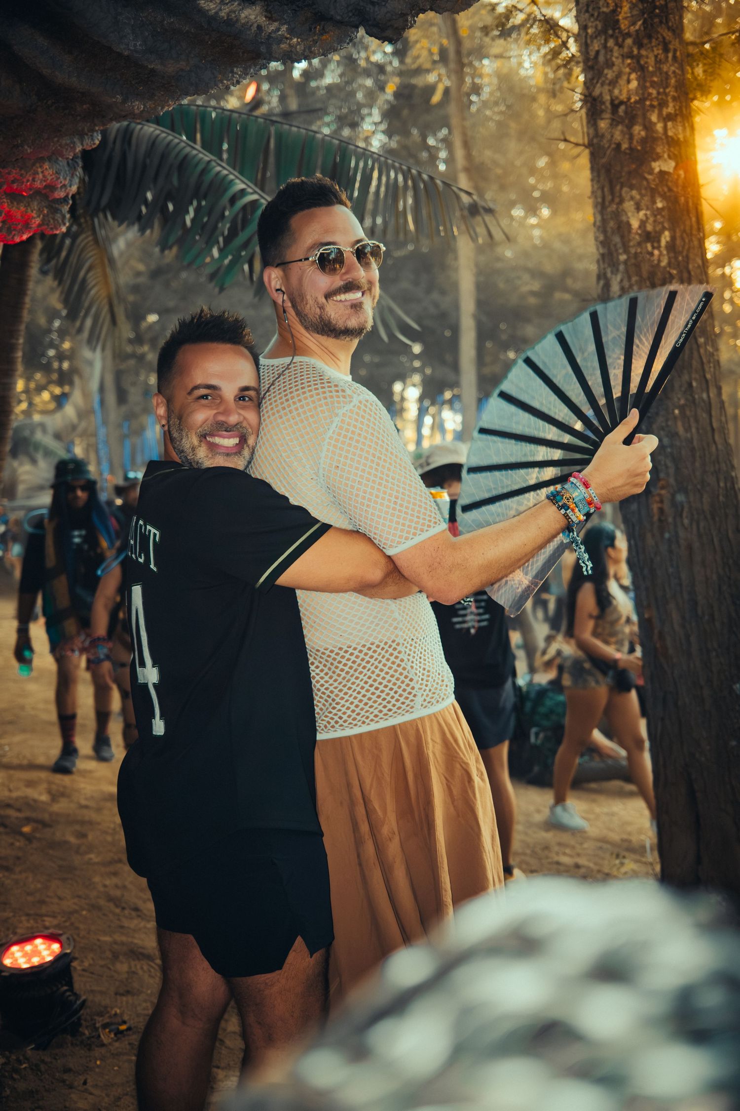 Two people dancing together outdoors at sunset while holding decorative fans in a natural forest setting.