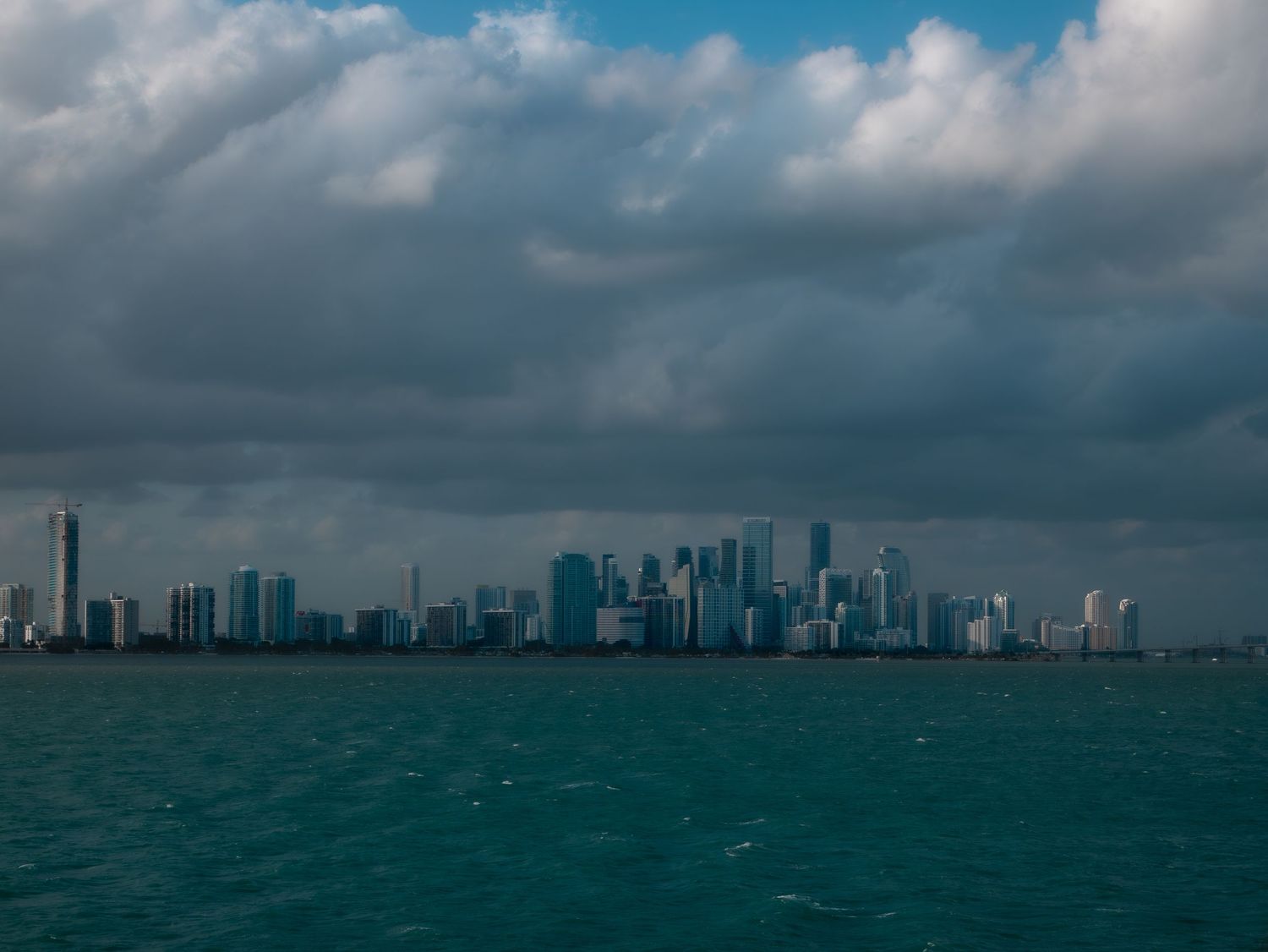 Dramatic stormy skyline of Miami viewed from Biscayne Bay with dark clouds looming over turquoise waters.