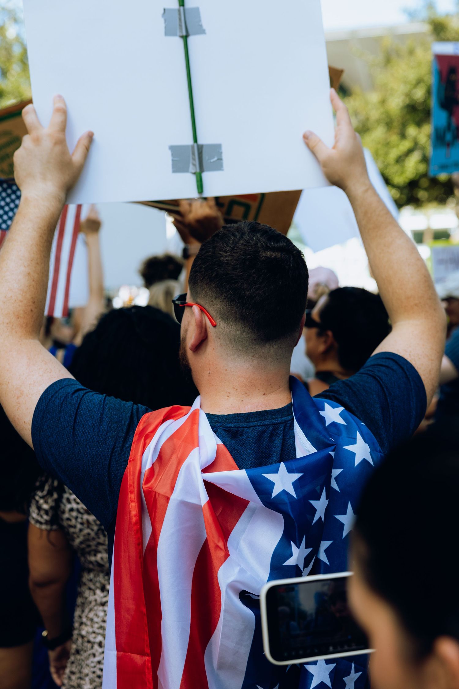 Protester wearing American flag attire holds sign at demonstration.