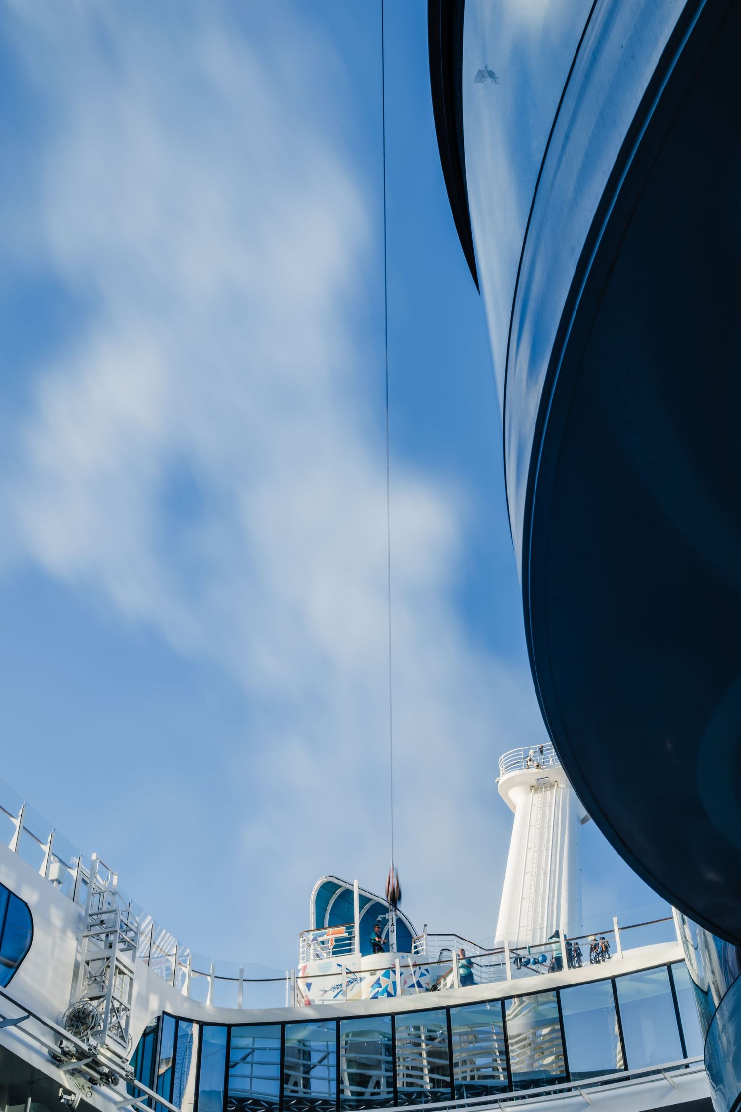 Looking up at cruise ship's white radar equipment and communication towers against blue sky with fluffy clouds.