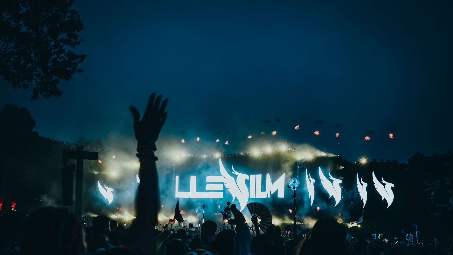 Illenium performing live at an outdoor music festival with dramatic fog and blue stage lighting.