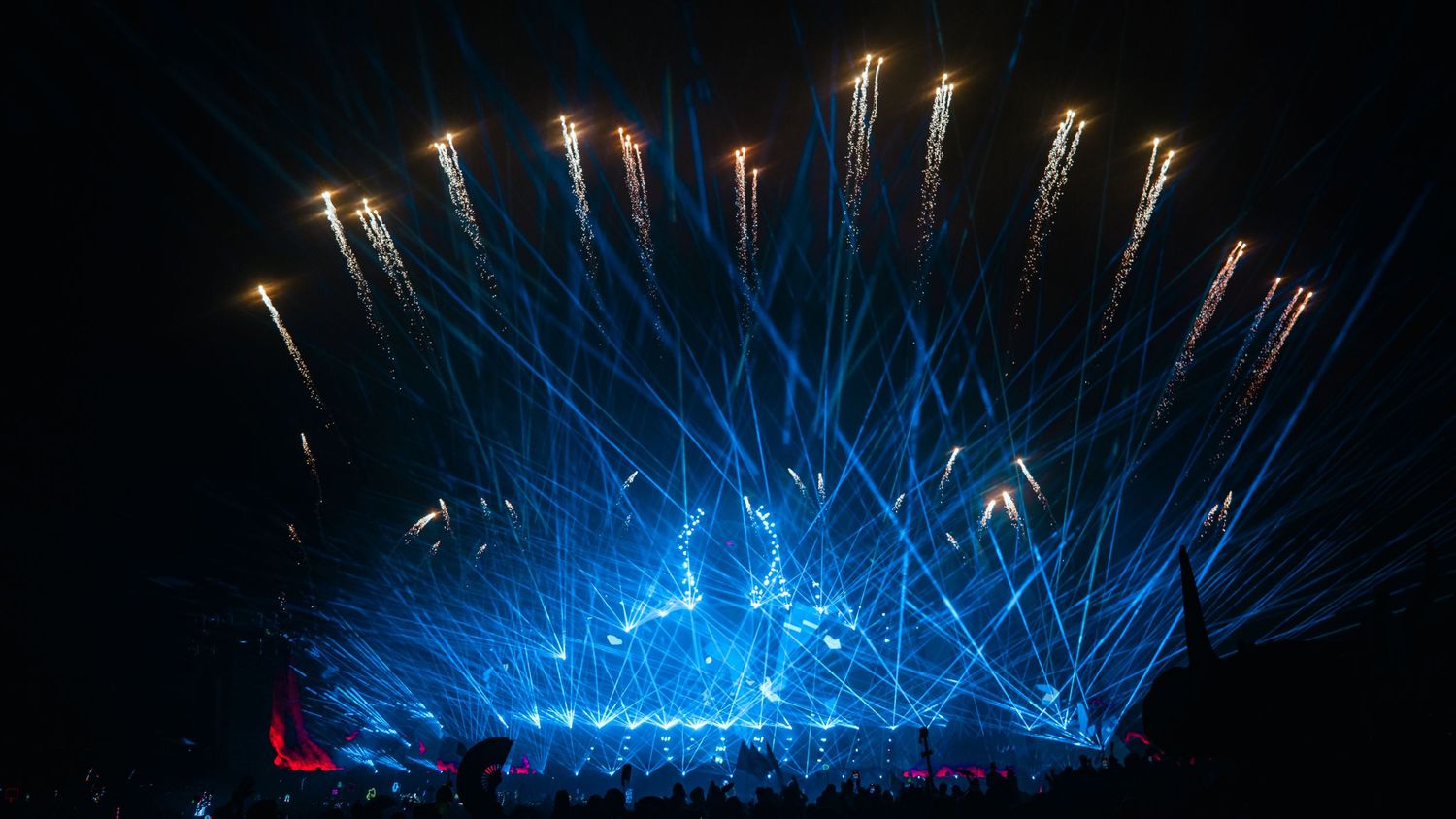 Bright blue laser beams illuminate a dark night sky during an outdoor light show performance.