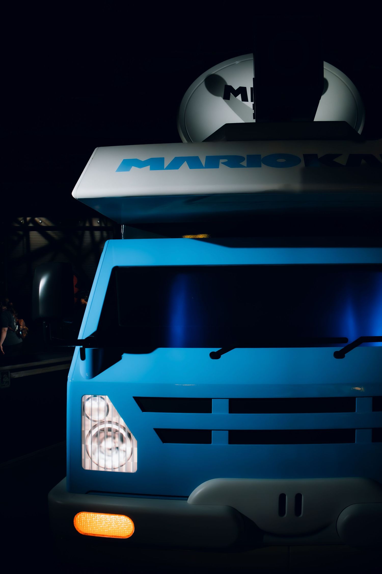 Close-up of a blue commercial Marka truck front grille and headlights illuminated in dark lighting conditions.