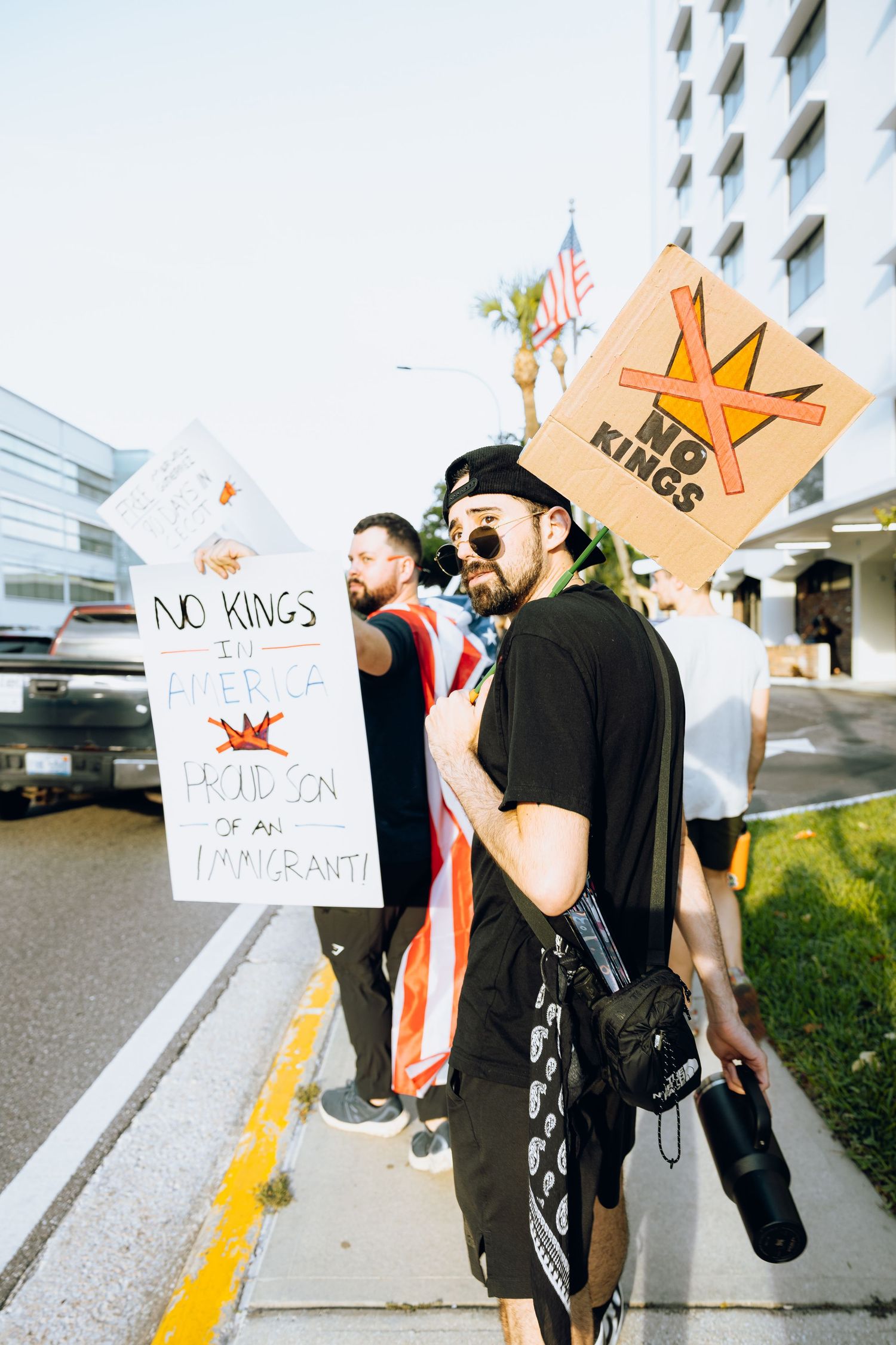 Protesters with 'No Kings' signs gather on a city sidewalk during a demonstration.