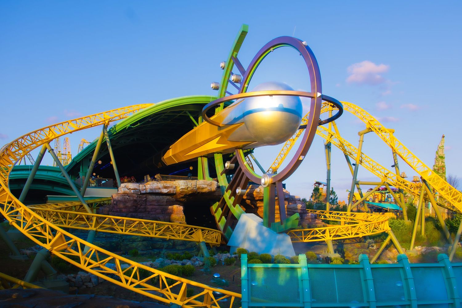 Yellow roller coaster track with futuristic spacecraft design element against blue sky at amusement park.