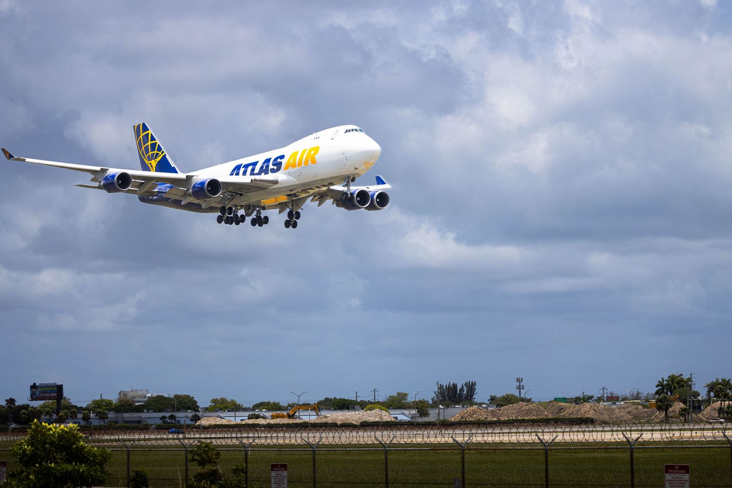 Atlas Air Boeing 747 cargo plane taking off against a cloudy sky at a busy international airport.