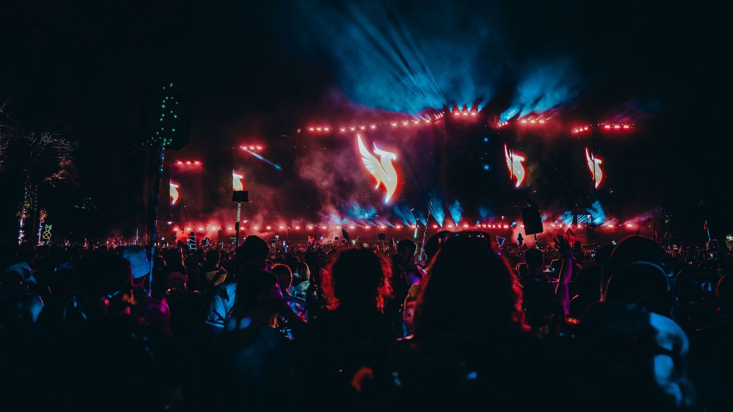 Concert crowd silhouettes against a dark backdrop with red stage lighting and smoke effects creating an atmospheric scene.
