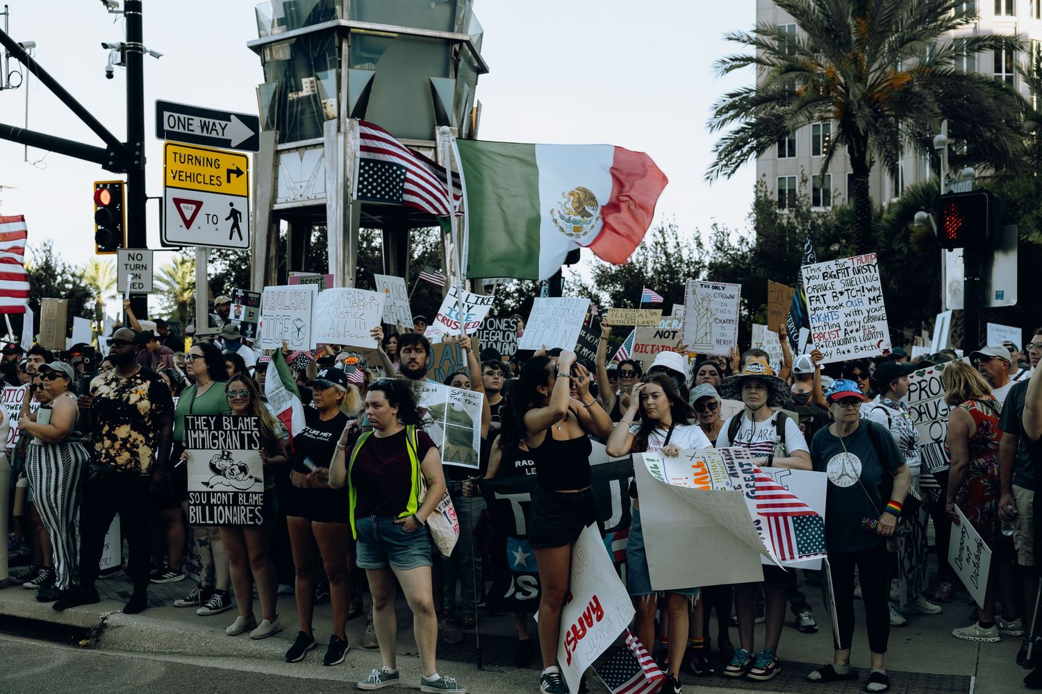 Demonstrators line city street holding protest signs and flags.