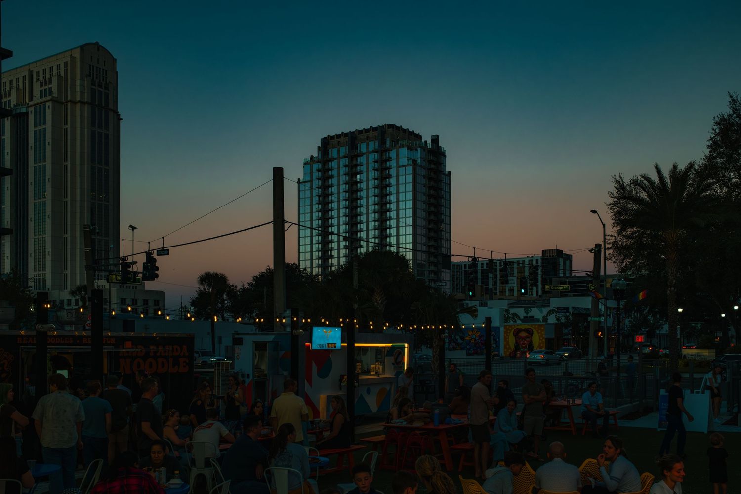 A panoramic cityscape view of high-rise buildings and palm trees silhouetted against a dusky sunset sky.