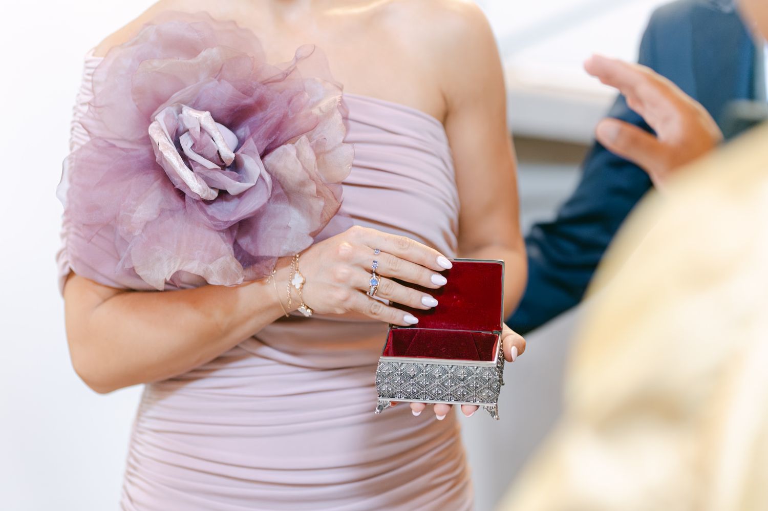 Bridesmaids hold elegant clutch purses and flower bouquets in soft purple and pink tones at a formal wedding.