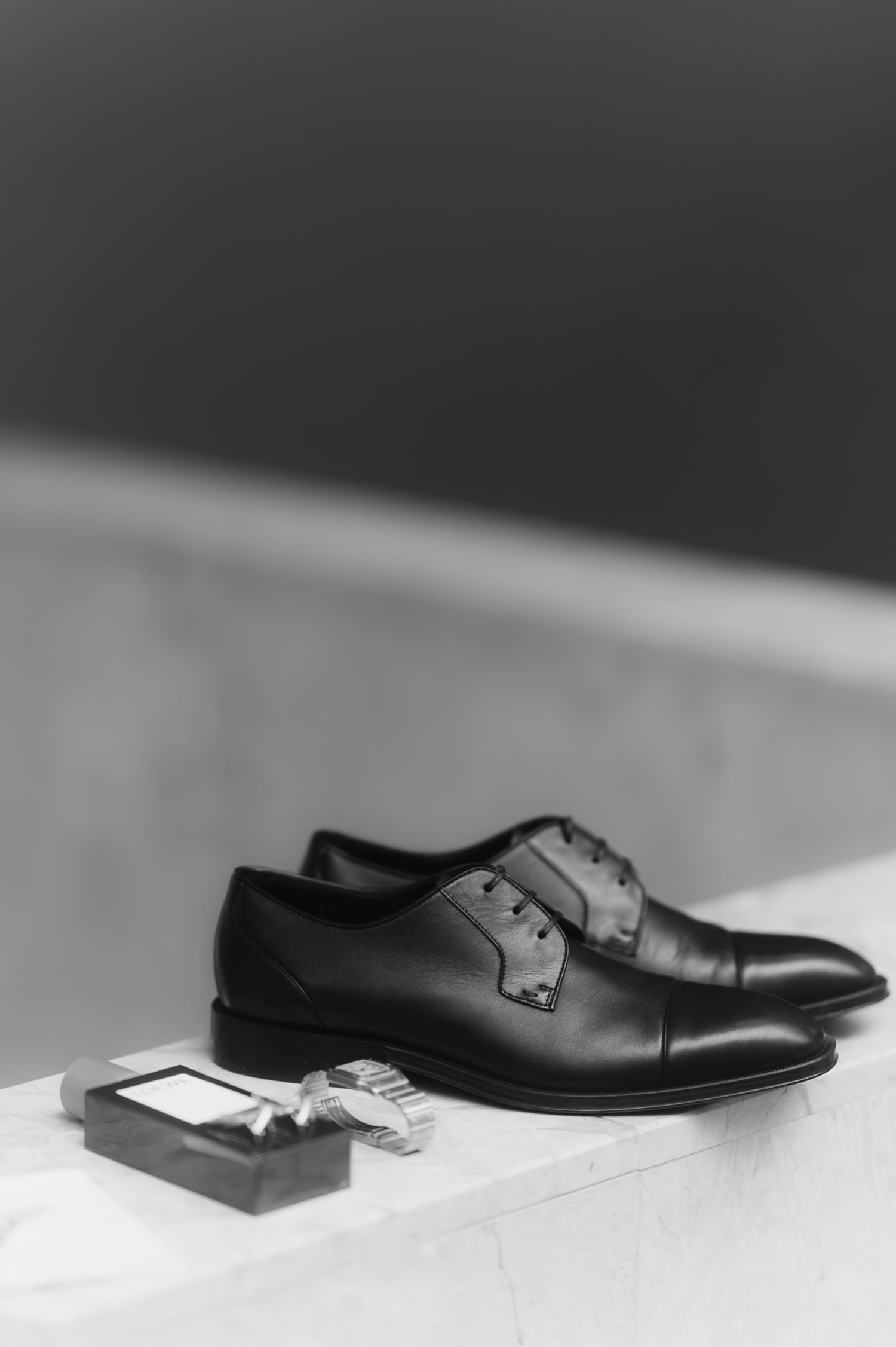 Black and white flat lay of classic black Oxford dress shoes and cufflinks for a wedding groom.