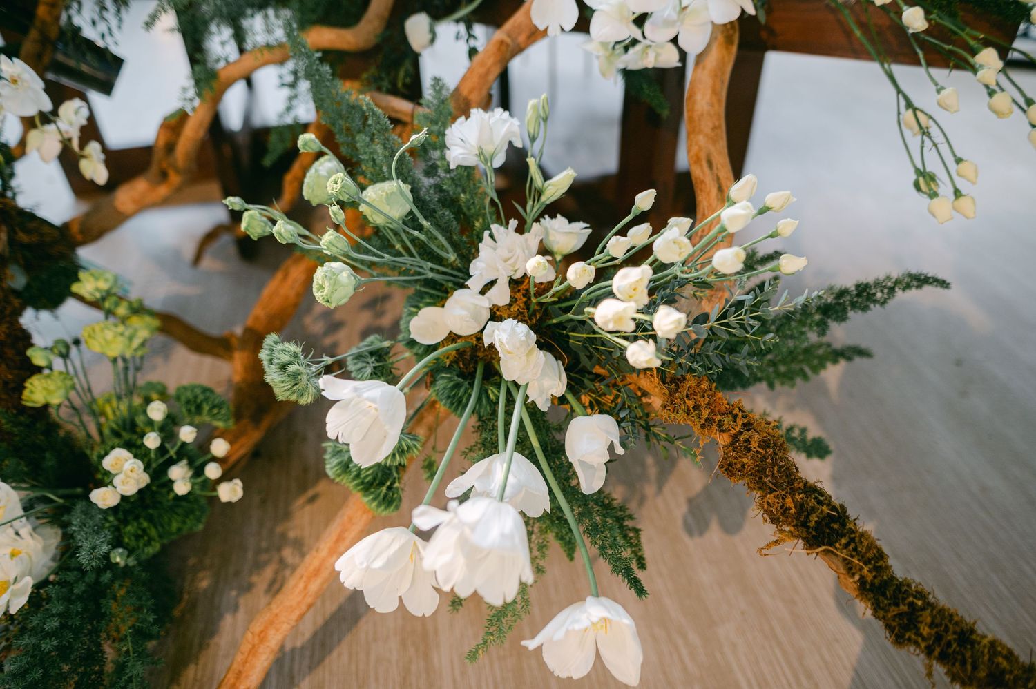 White tulips and ferns arranged on a rustic wooden centerpiece for a wedding table decoration.