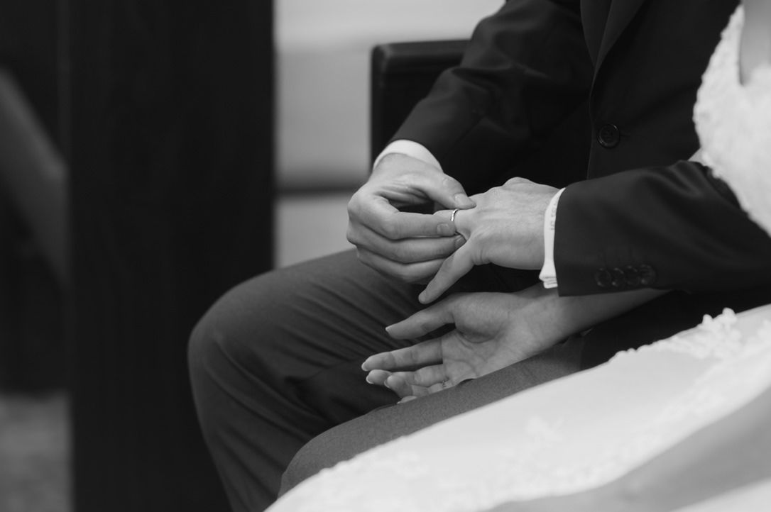 Black and white photo of hands clasped together during an intimate wedding ceremony moment.