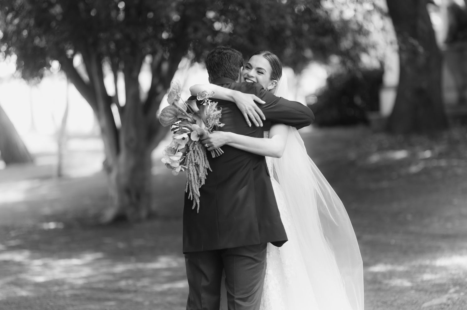 Black and white photo of bride and groom sharing an emotional first look hug outdoors.