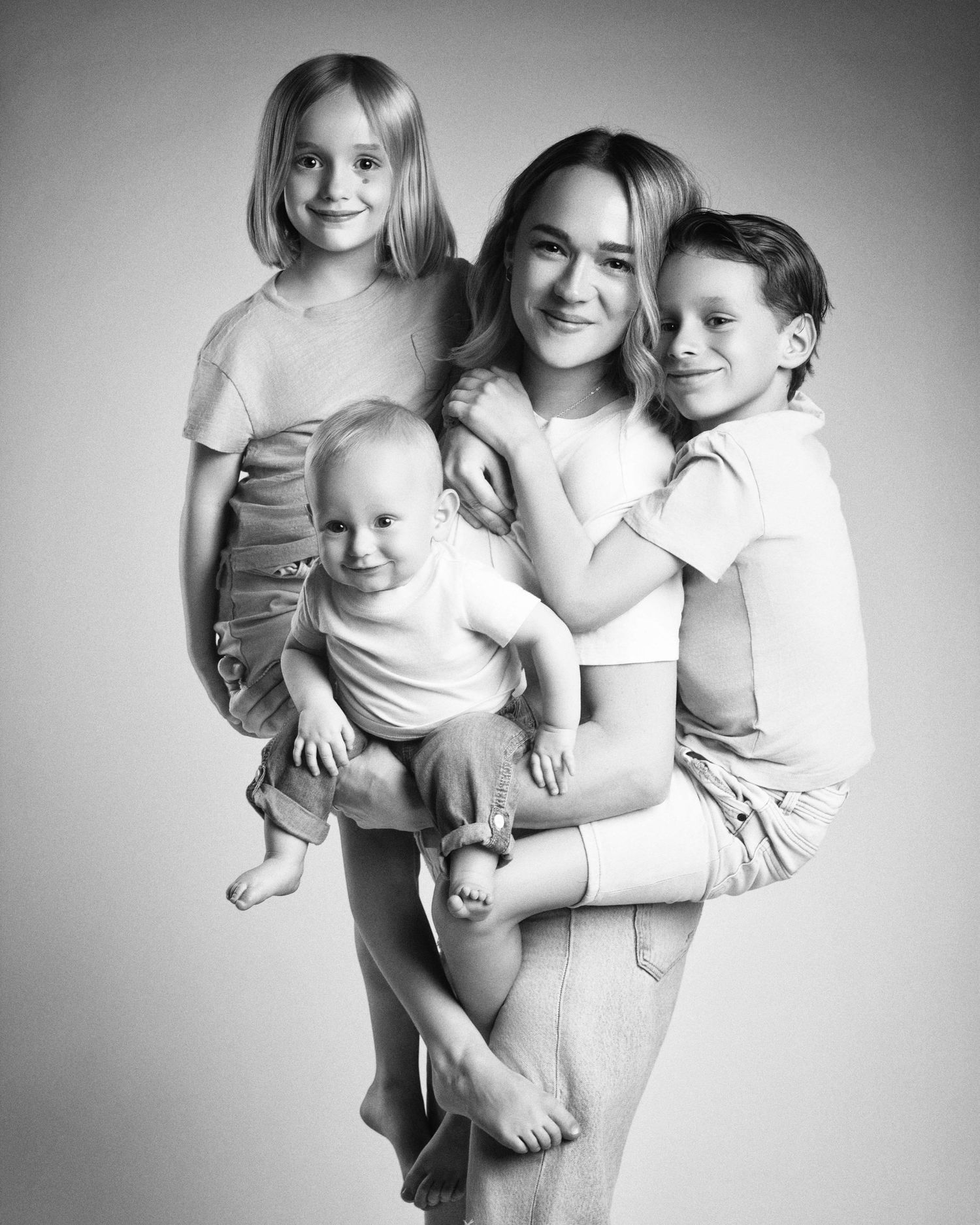 Black and white portrait of a mother holding three children, including a smiling baby, in a studio setting.