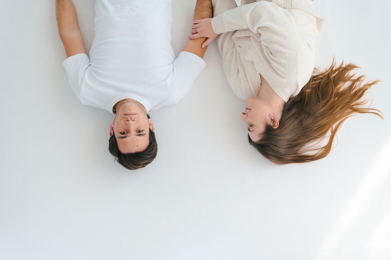 Aerial view of a couple lying on a white floor, heads together, wearing white and cream outfits.