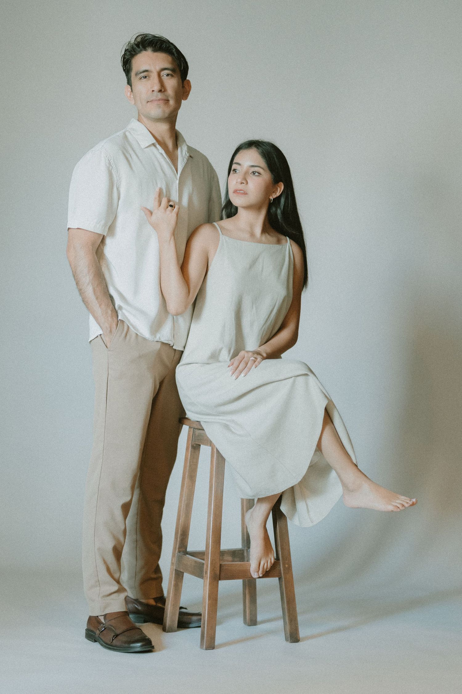 Man and woman posing together in neutral tones against a light background in a studio portrait session.