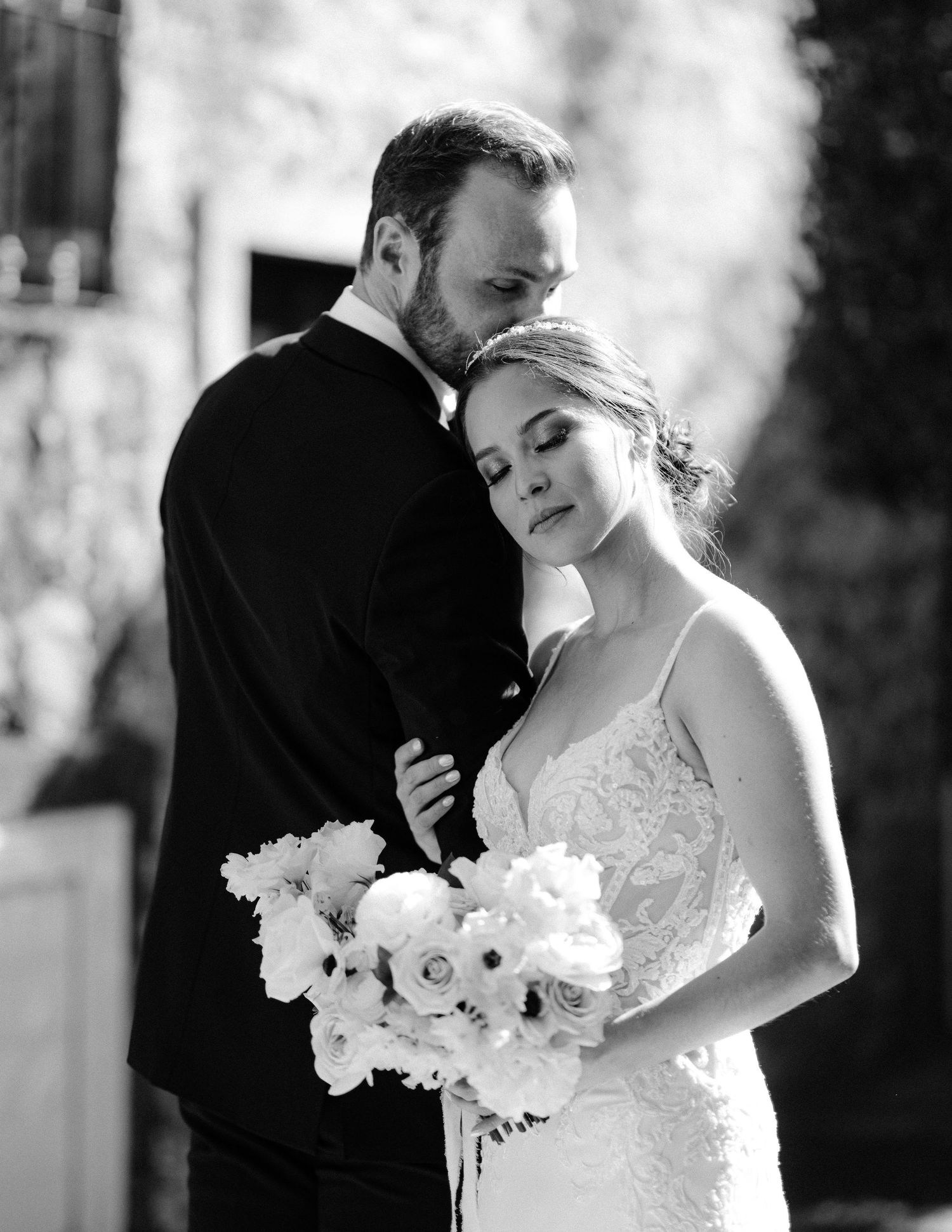 Black and white portrait of a bride and groom embracing, bride holding a white floral bouquet.