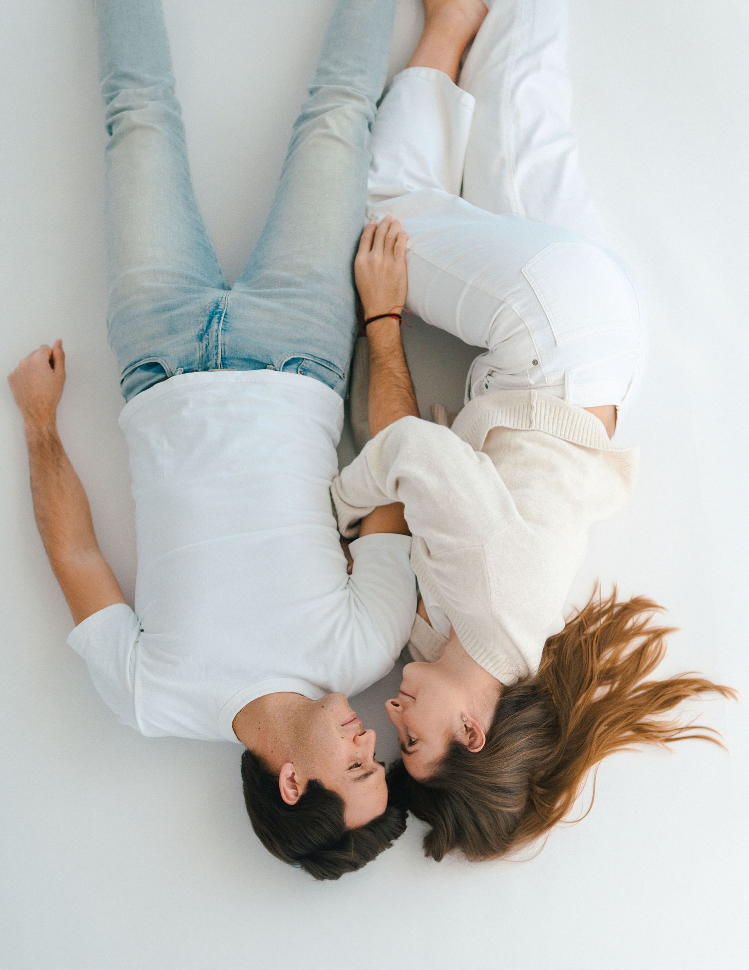 Couple lying on a white floor facing each other in coordinating light blue and white casual outfits.