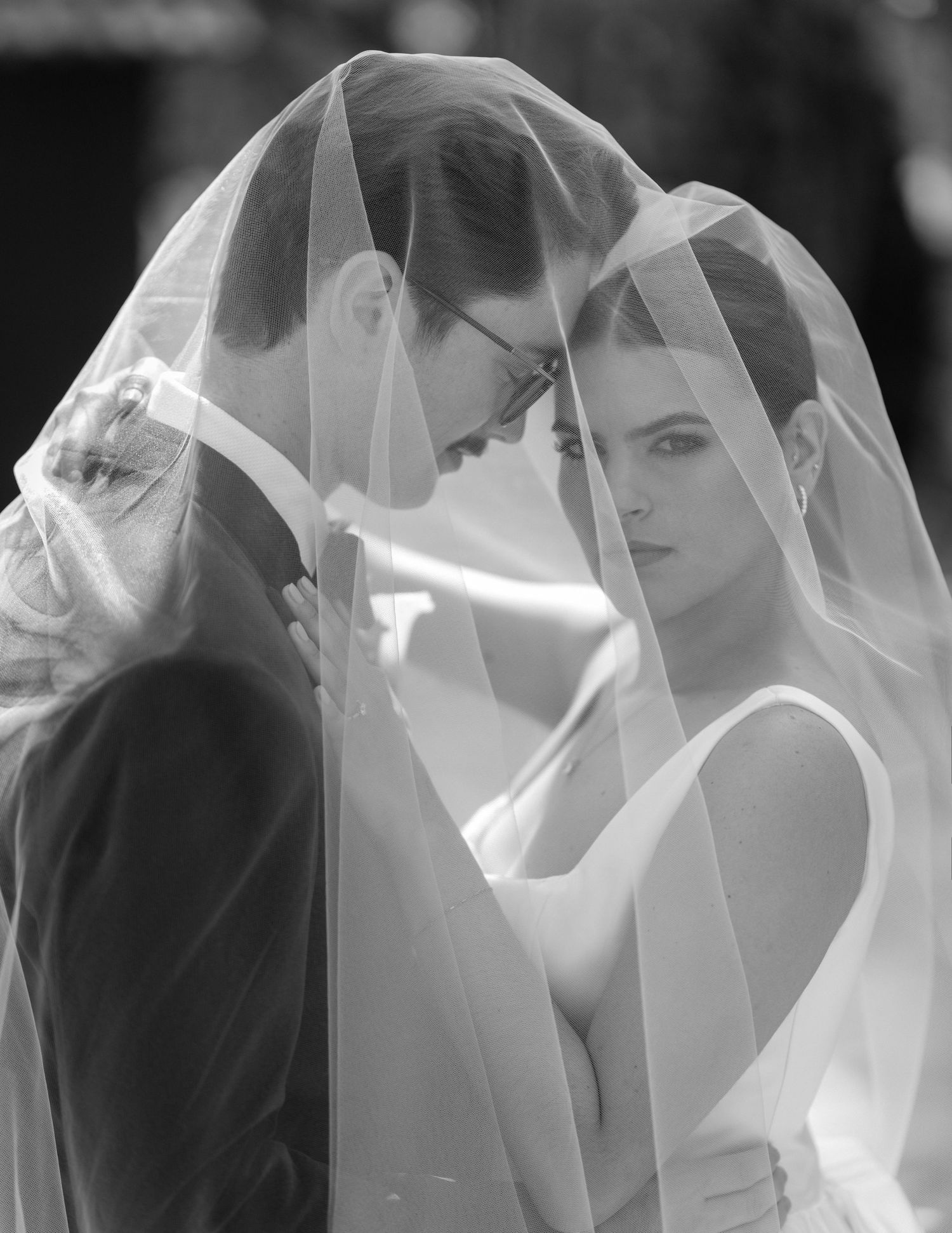 Romantic black and white portrait of bride and groom sharing an intimate moment beneath a flowing veil.