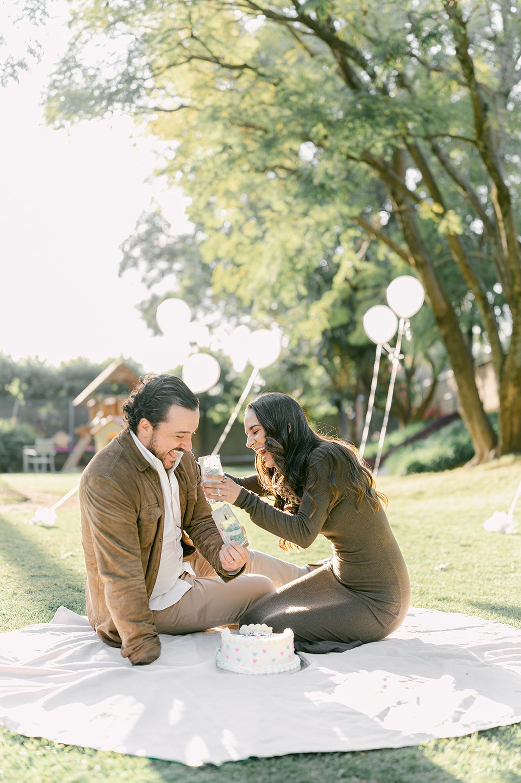Happy couple sitting on blanket cutting gender reveal cake together in sunny park.