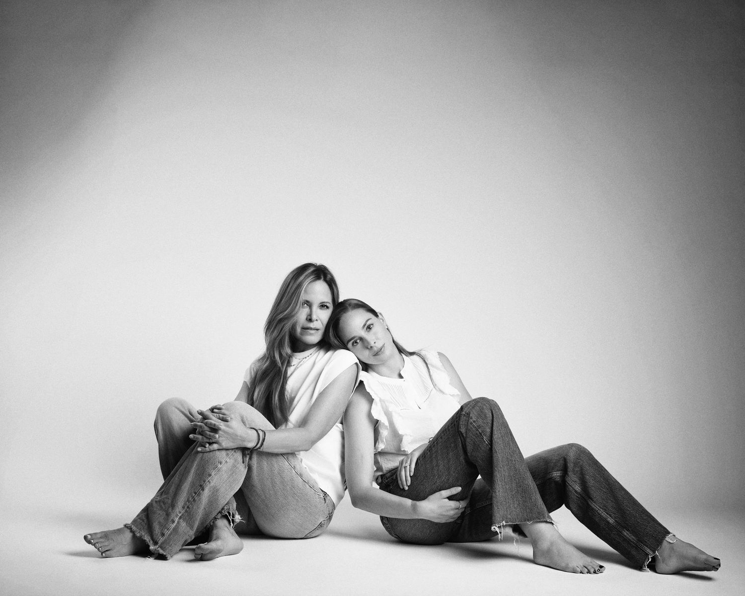 Two women lean together on the floor in a candid black and white studio portrait.