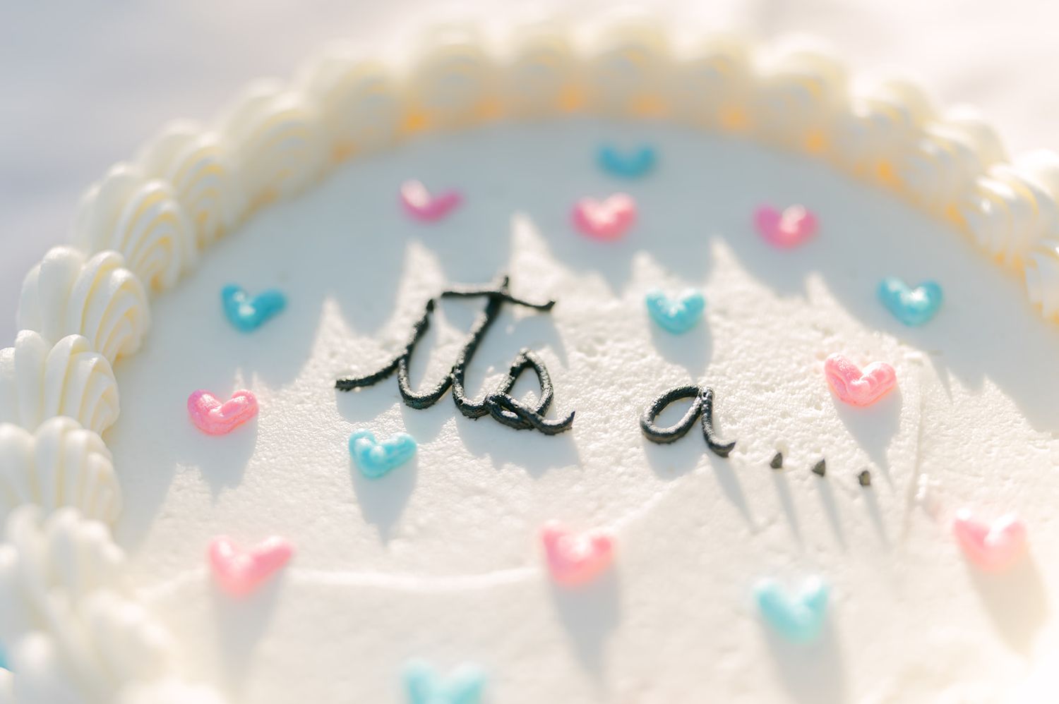 White gender reveal cake with pink and blue hearts and 'It's a...' written in black frosting.