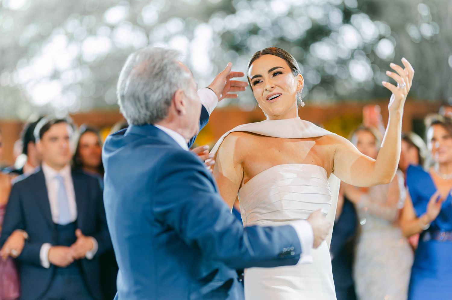 Smiling bride in strapless white gown dances joyfully with a guest at her wedding reception.