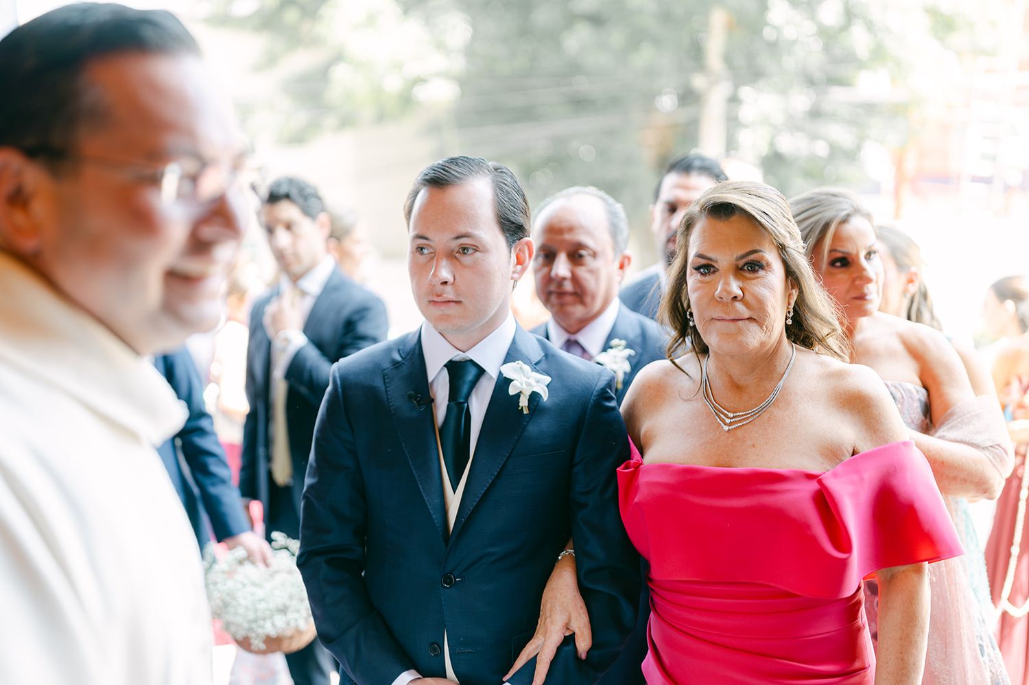 Groom in navy suit walks with woman in pink off-shoulder dress down wedding ceremony aisle.