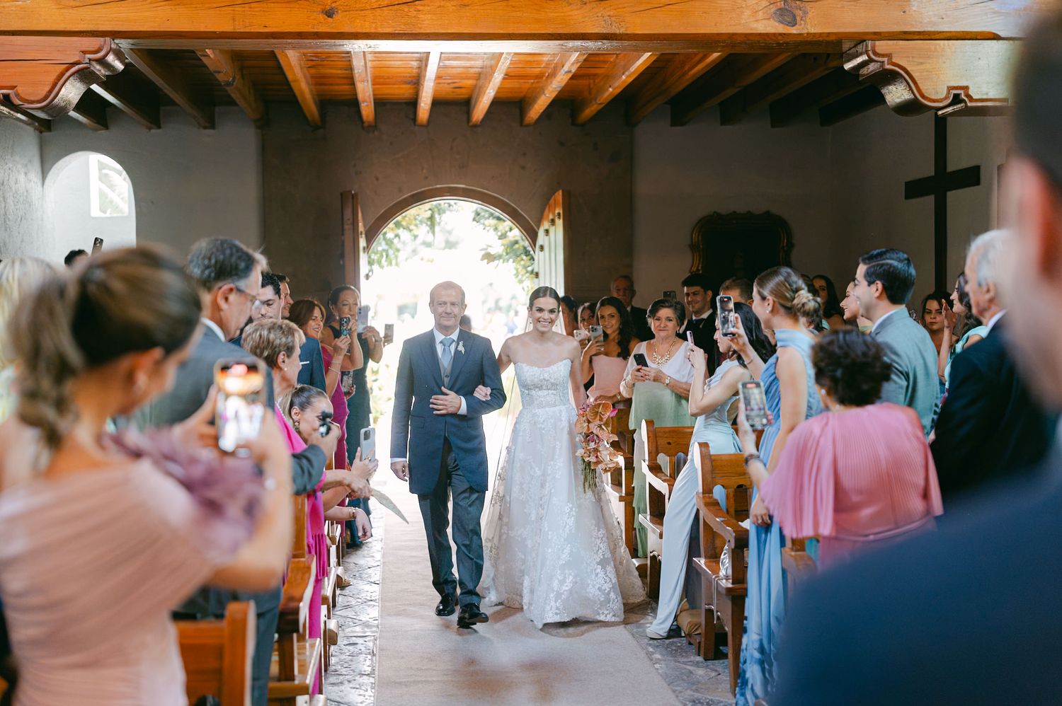 Guests observe a wedding ceremony through a rustic wooden archway in an intimate venue.
