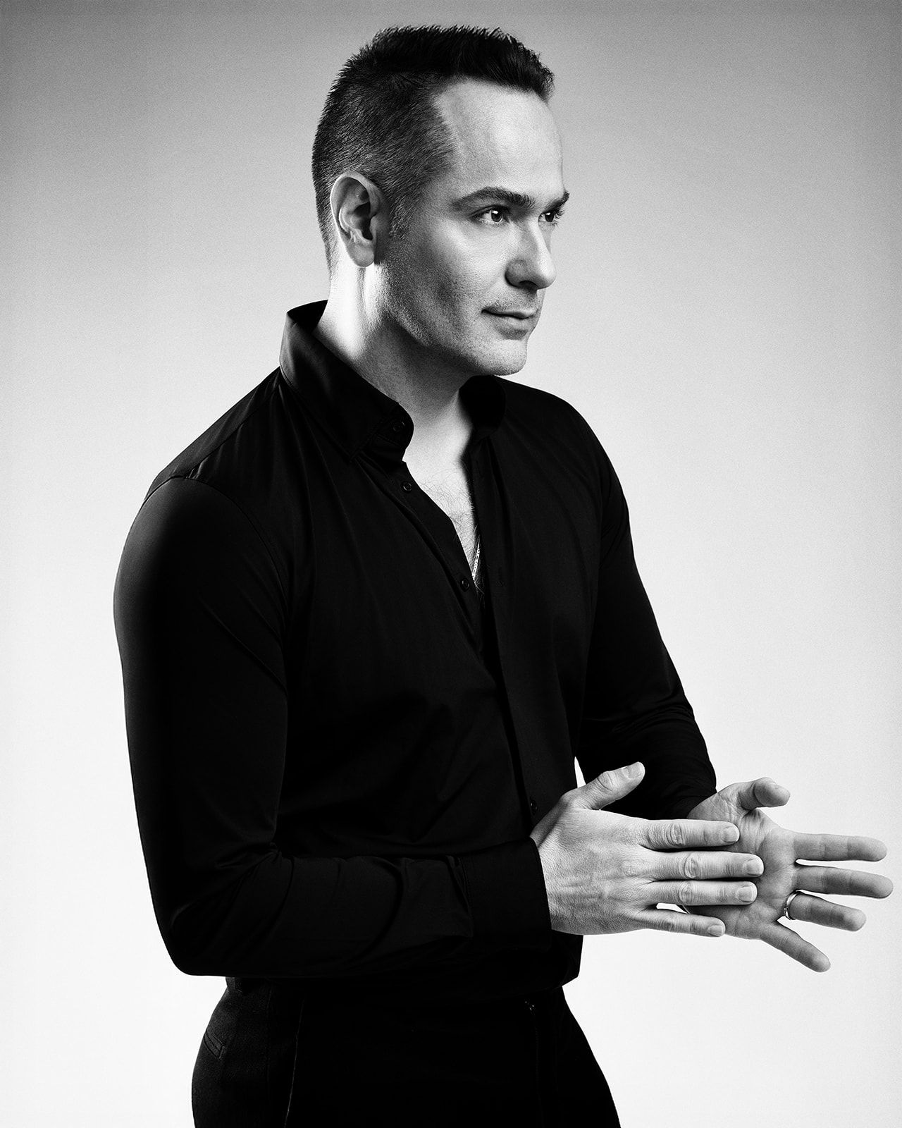 Close-up black and white portrait of a man in black shirt with hands clasped together.