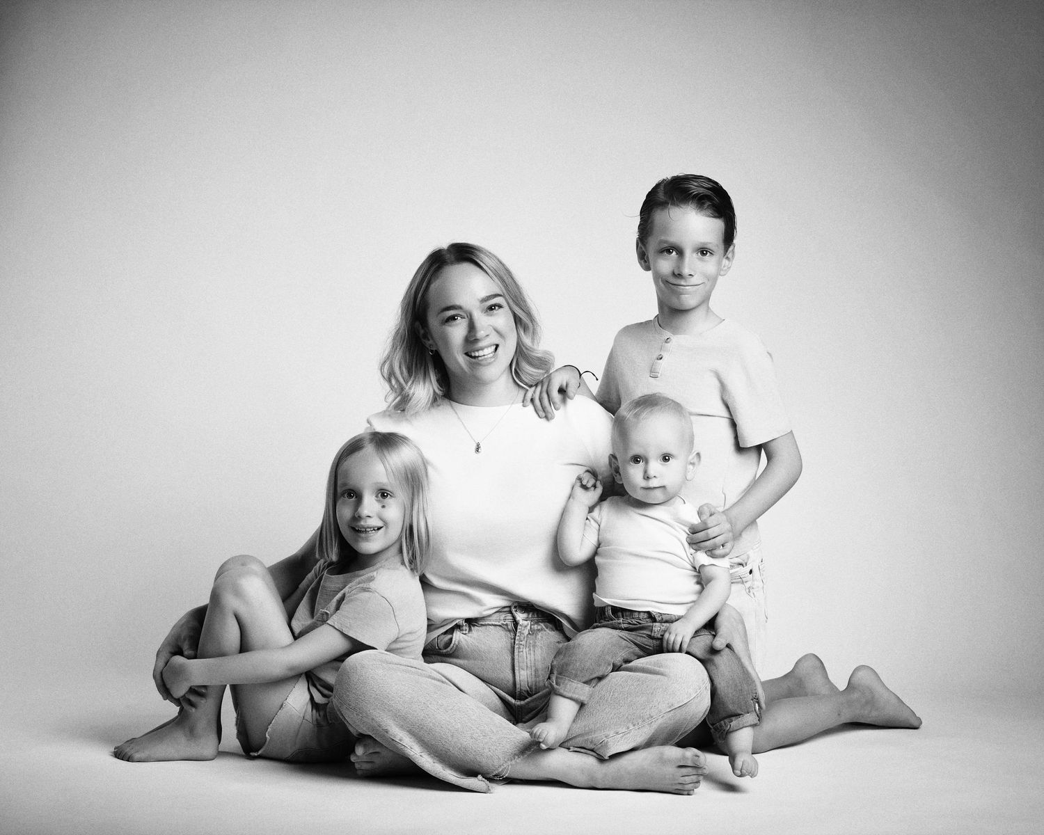 Black and white studio family portrait of a mother sitting on the floor with three children including a baby.