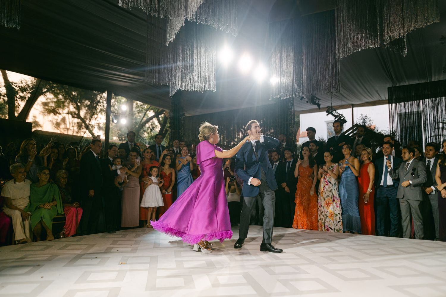 Dancers in formal attire perform on a white dance floor under dramatic lighting at a wedding reception.