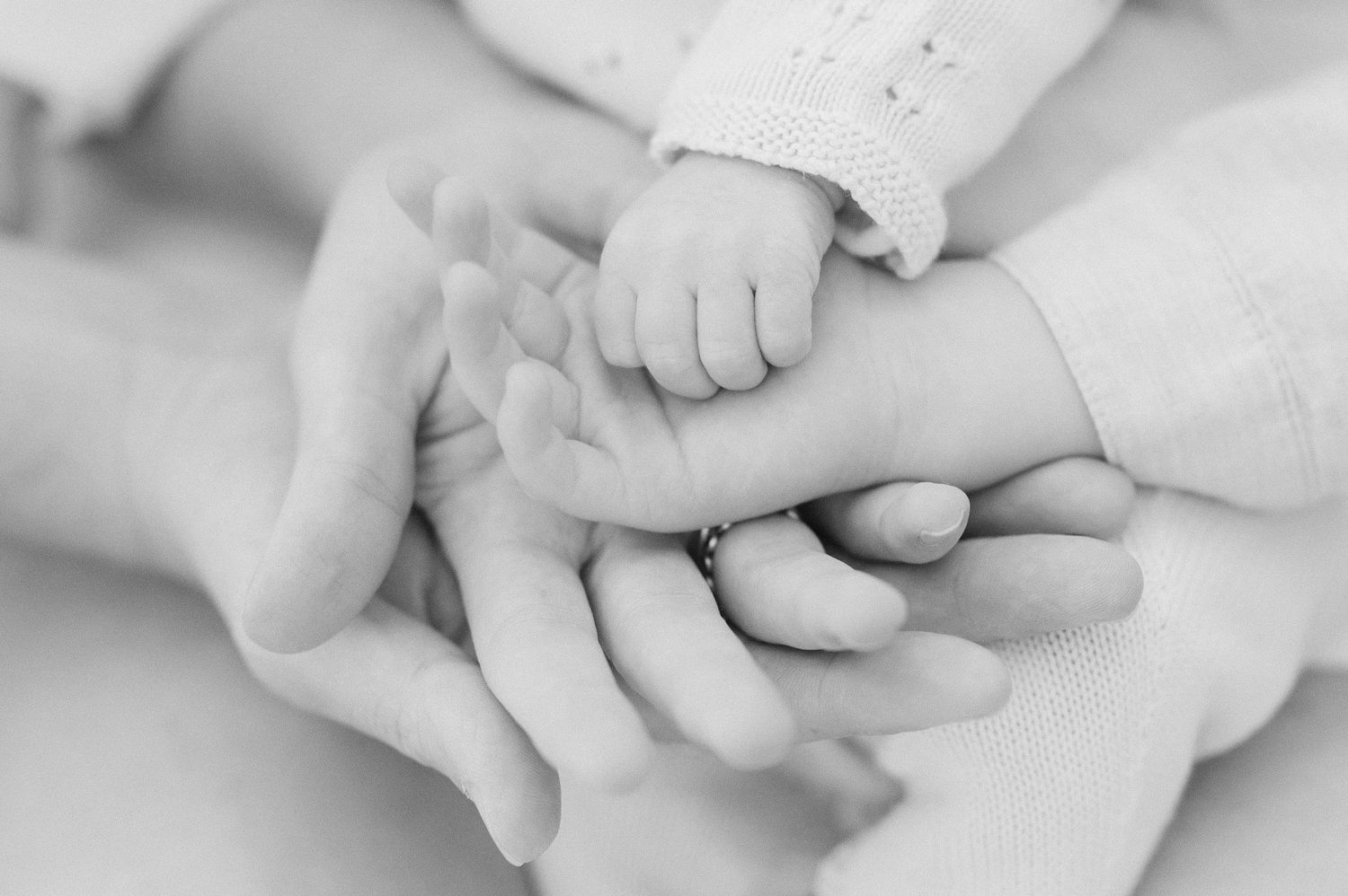 Black and white close-up of a newborn's tiny hand resting on parents' hands.