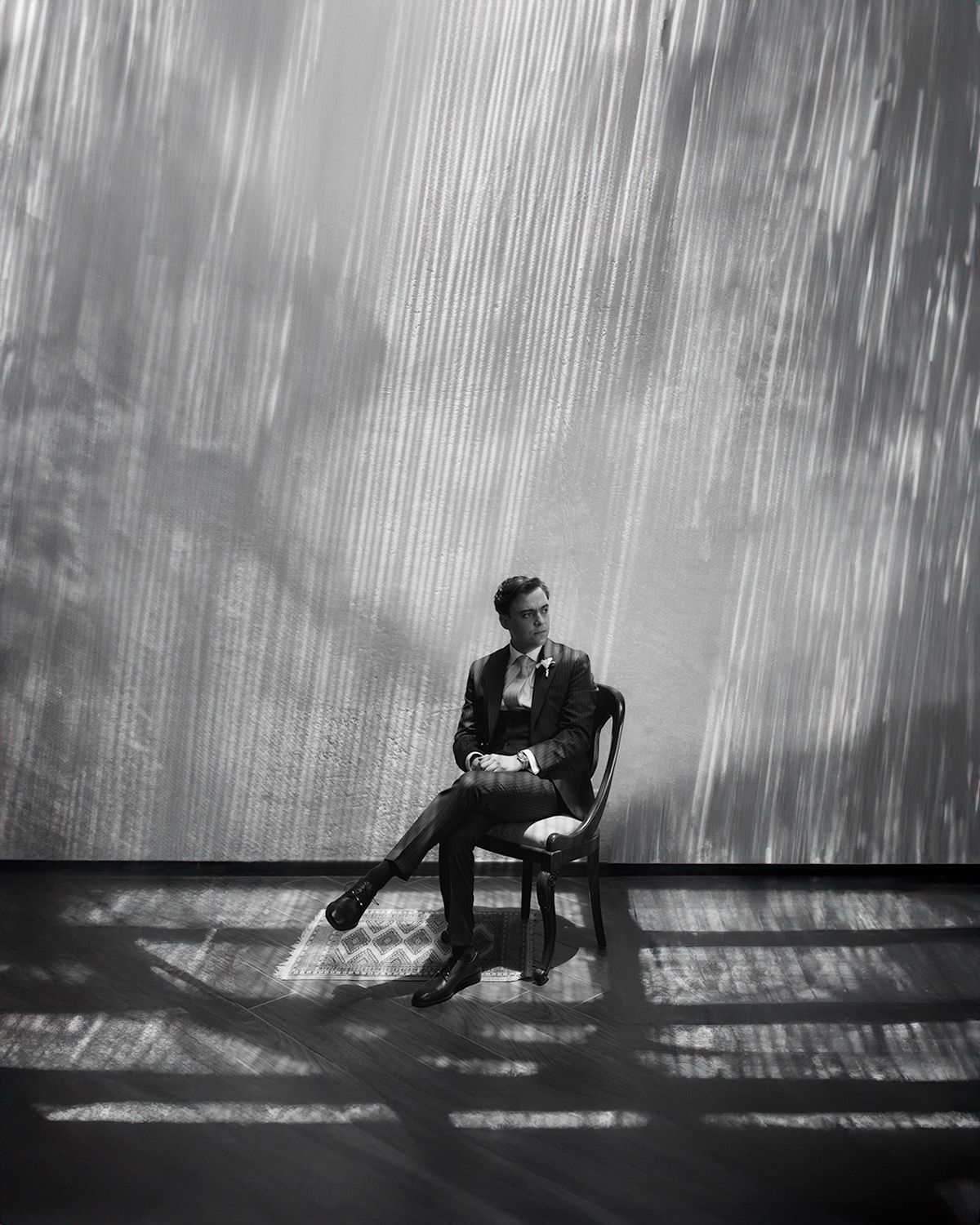 Groom in tuxedo seated on chair in dramatic black and white light streaks portrait.
