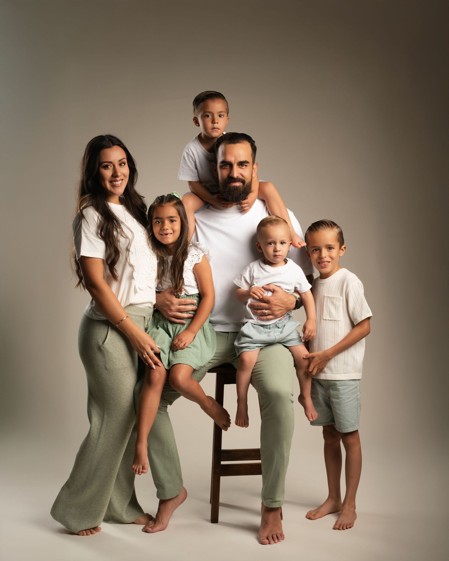 Studio family portrait of parents with four young children in coordinated white and green outfits.