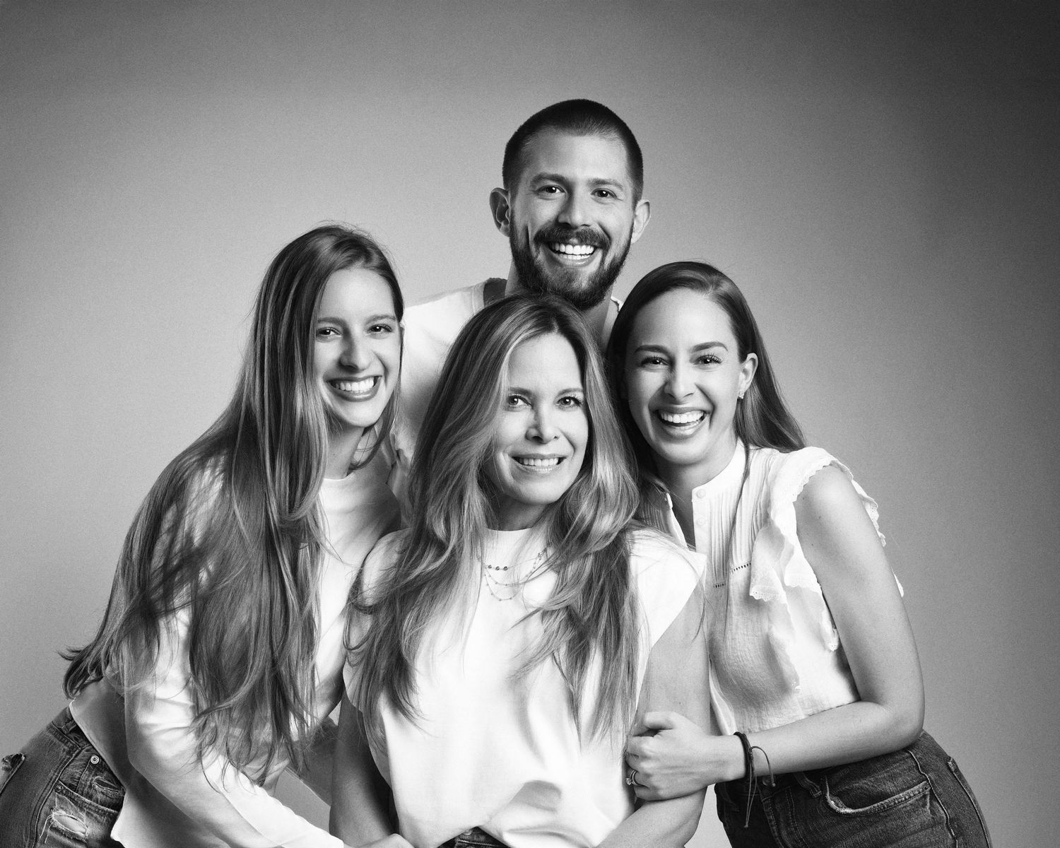Black and white studio portrait of a happy family of four, two young women with parents smiling together.