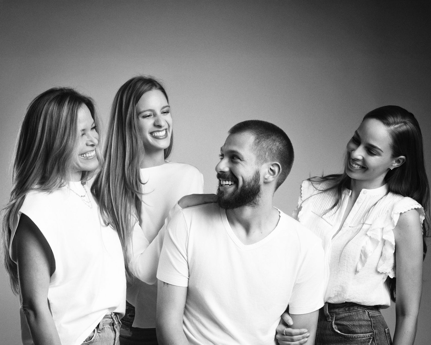 Four people laugh together in a lively black and white studio group portrait.