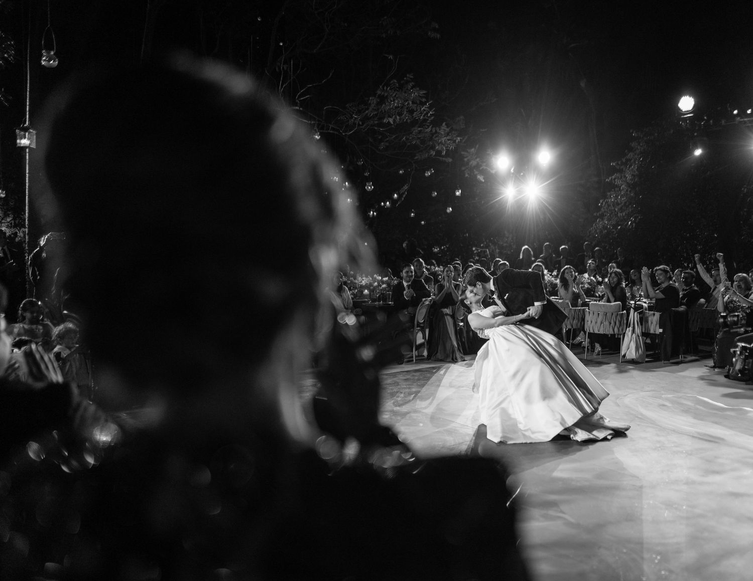 Black and white photo of a couple sharing their first dance surrounded by cheering wedding guests.