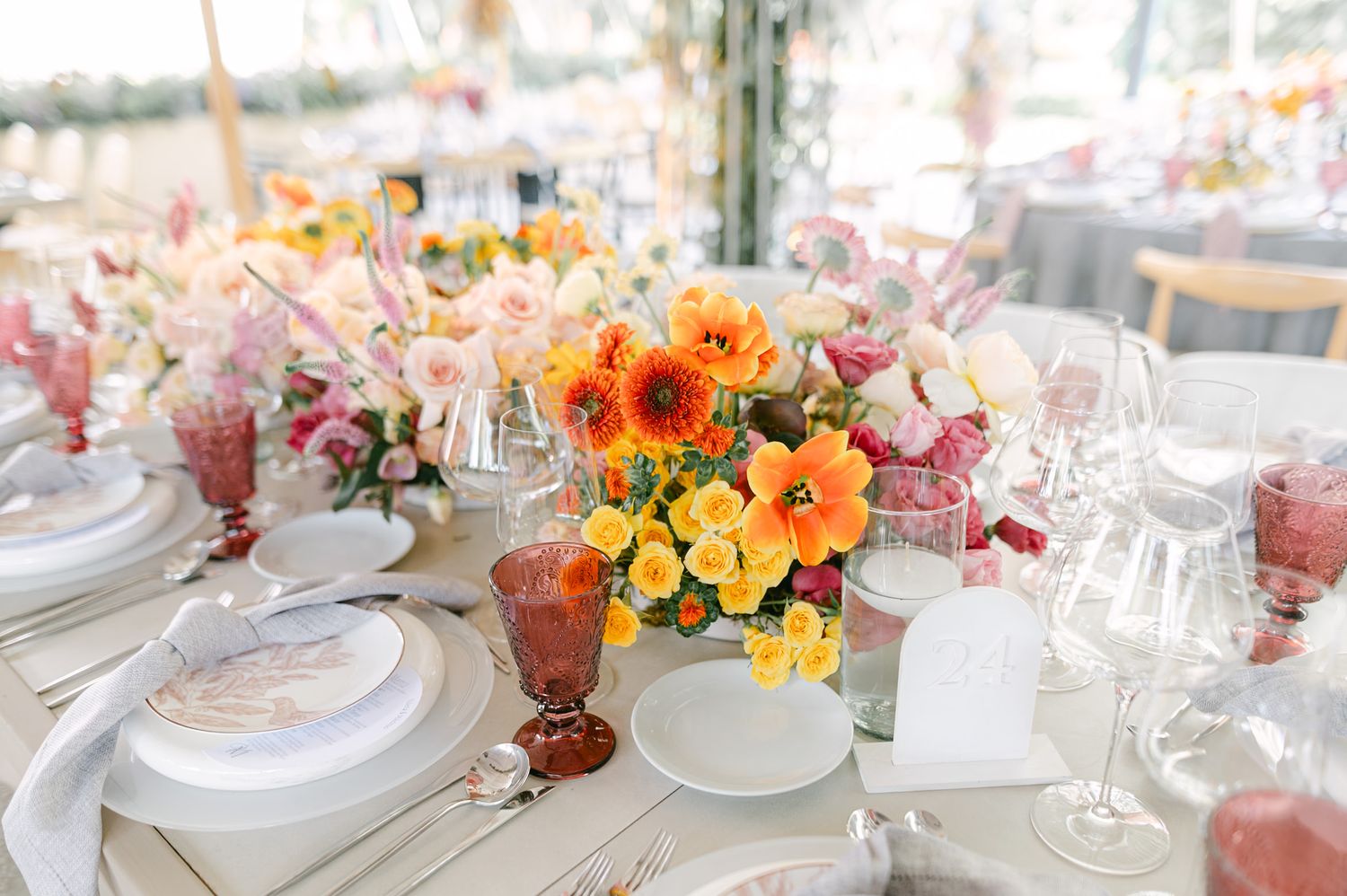 Vibrant wedding table centerpiece featuring orange poppies, yellow roses, and pink blooms with amber glassware.