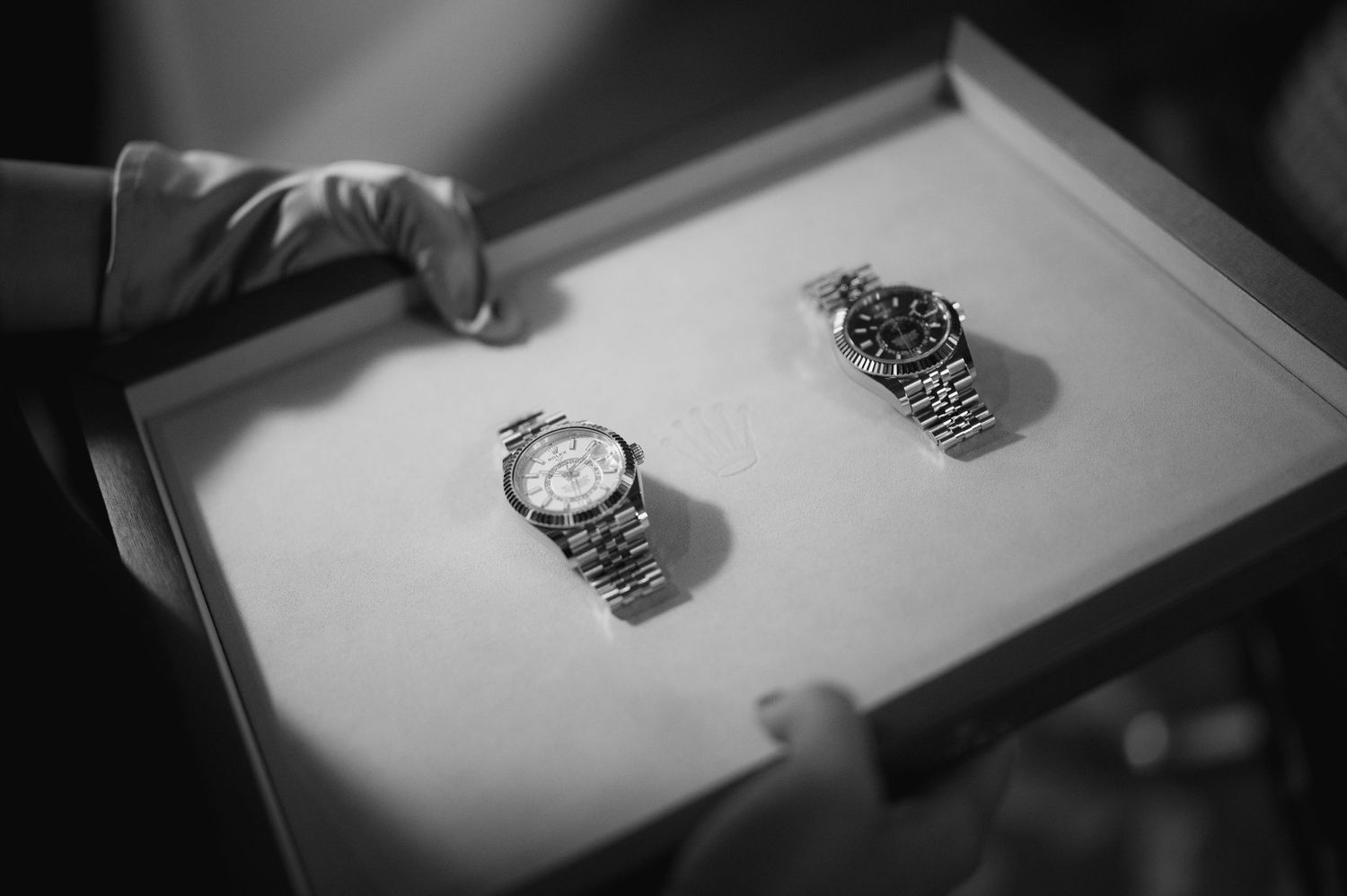 Black and white photo of two matching luxury wristwatches presented on a white tray.