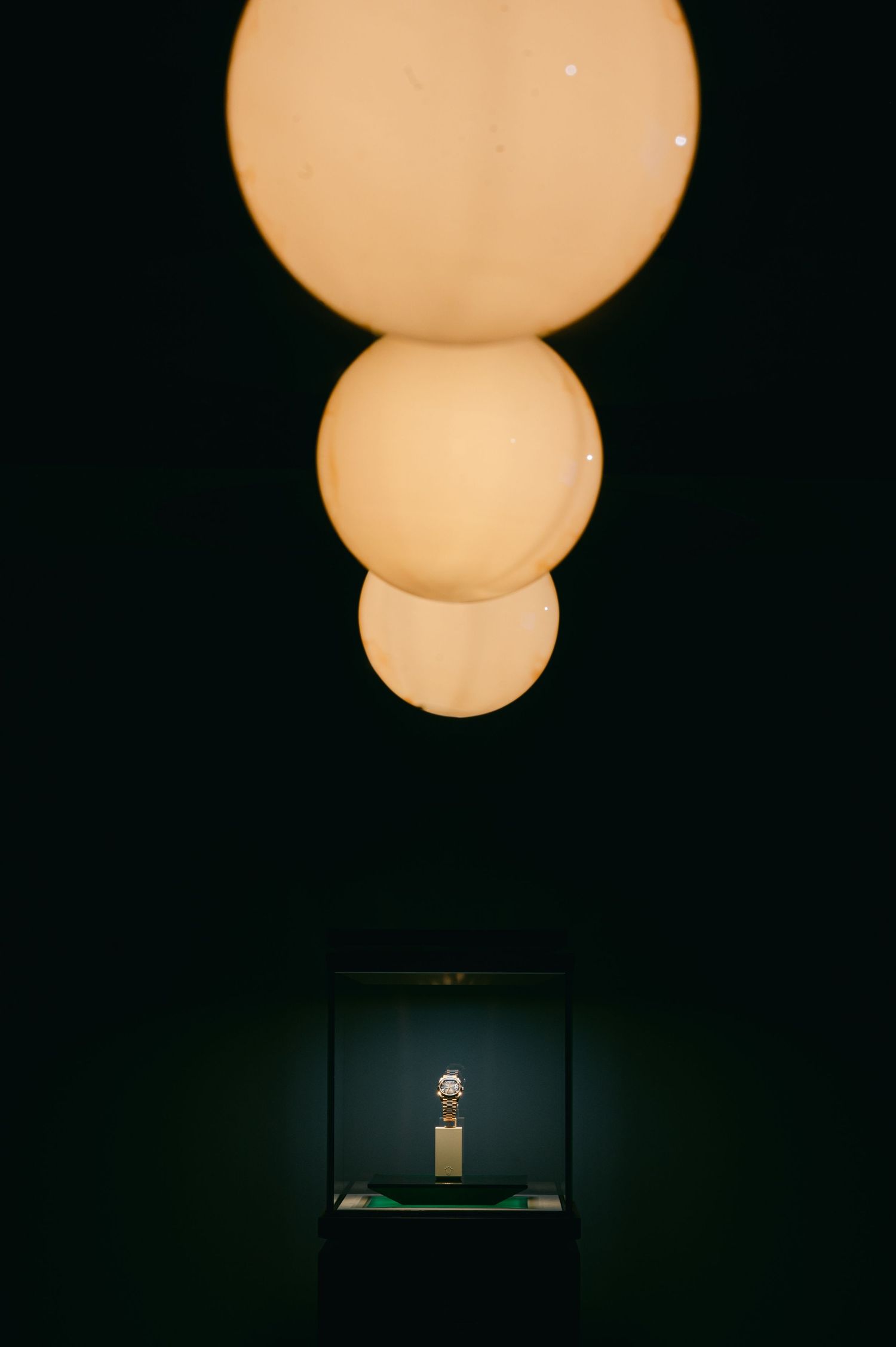 Glowing spherical pendant light fixture illuminating a display case with an artifact in a dark room.