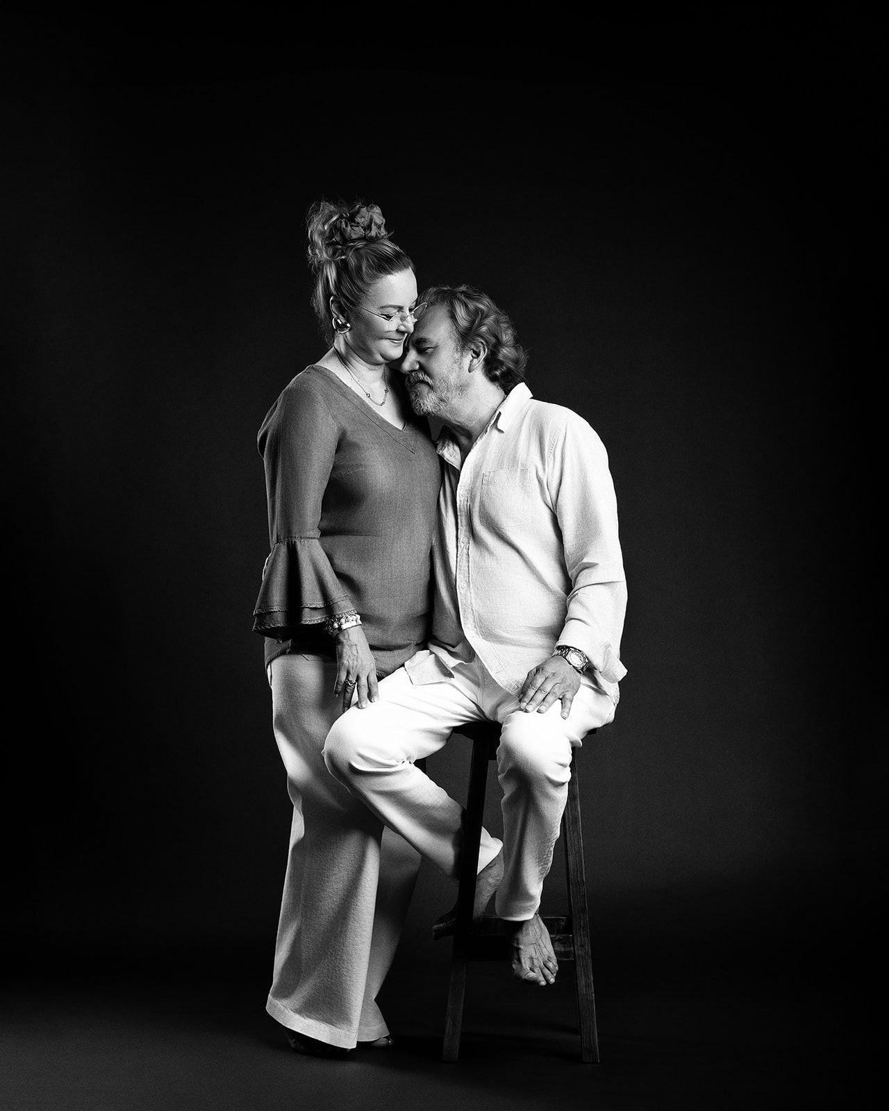 Black and white studio portrait of a pregnant woman and man sharing a tender moment.