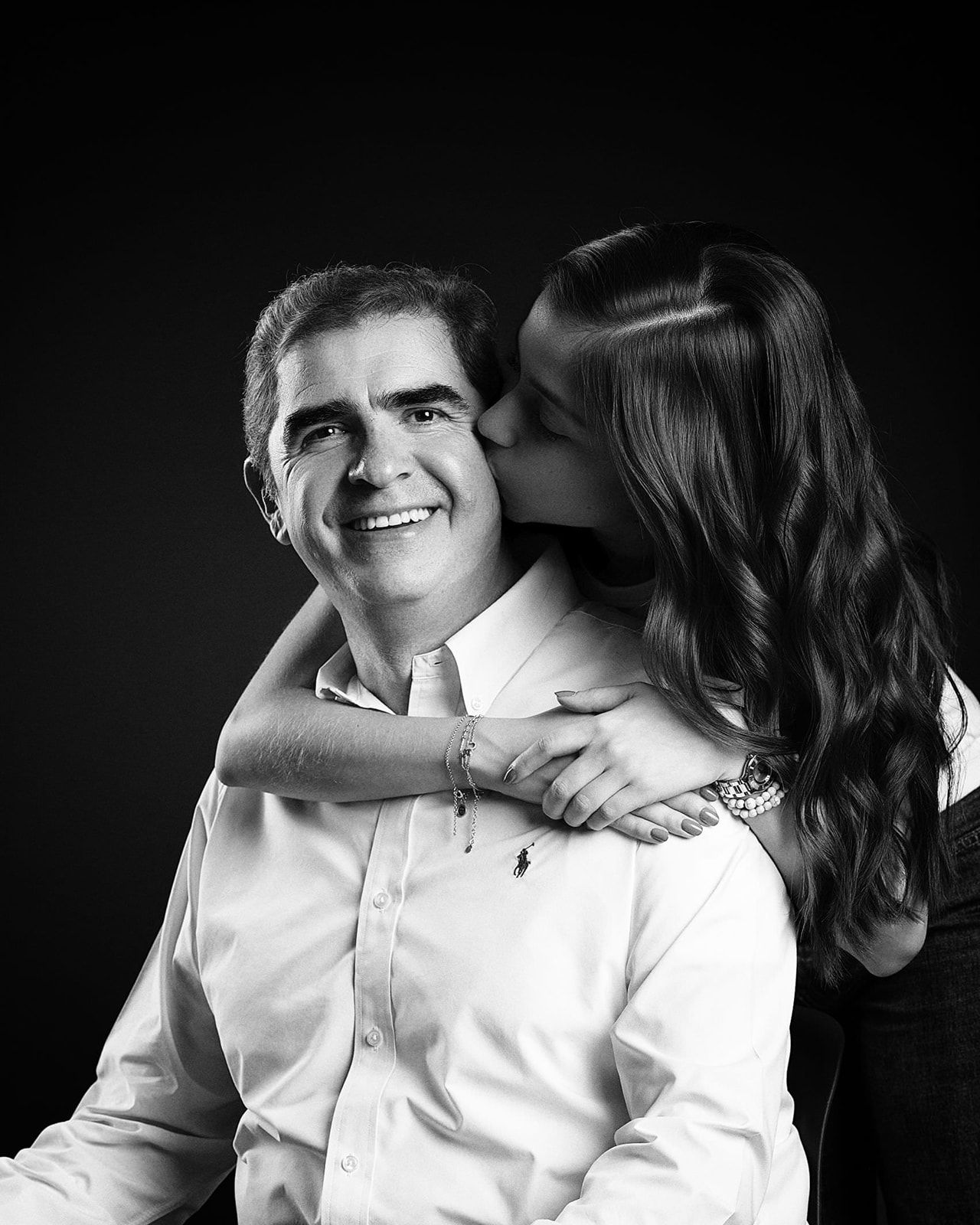 Black and white portrait of a smiling man receiving a kiss on the cheek from a young woman.