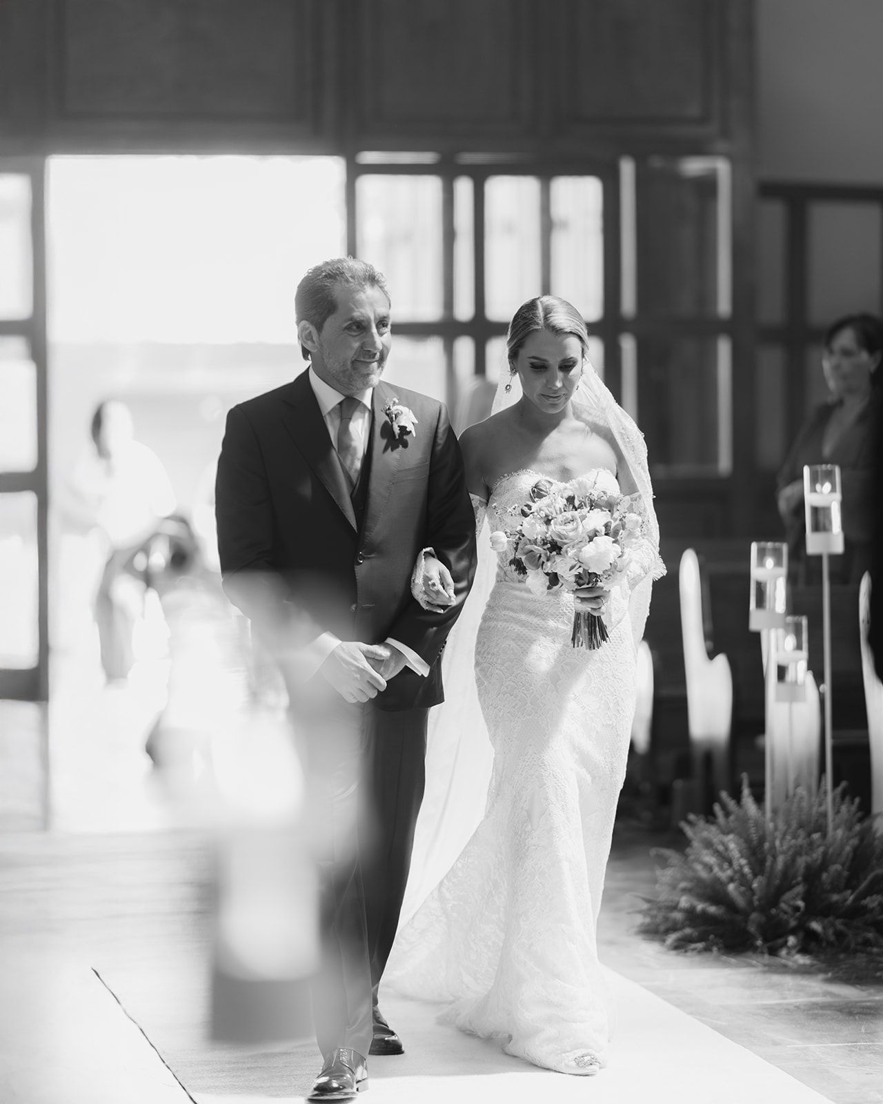 Bride walks down church aisle with father during traditional wedding ceremony procession.