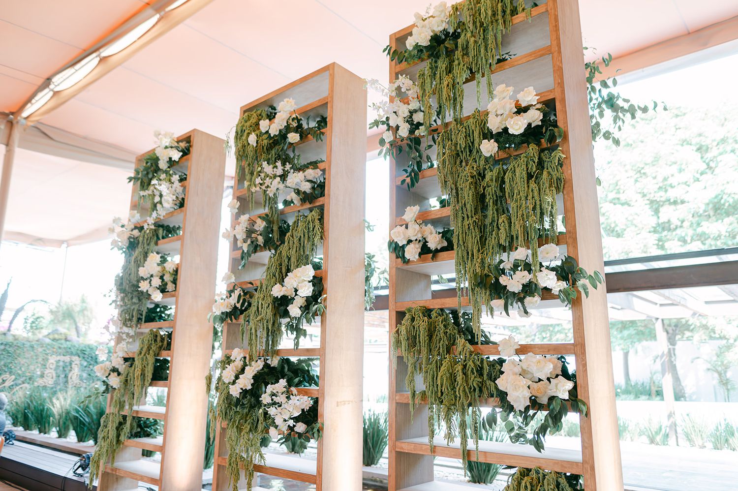 Elegant wooden shelving units adorned with cascading greenery and white floral arrangements at wedding venue.