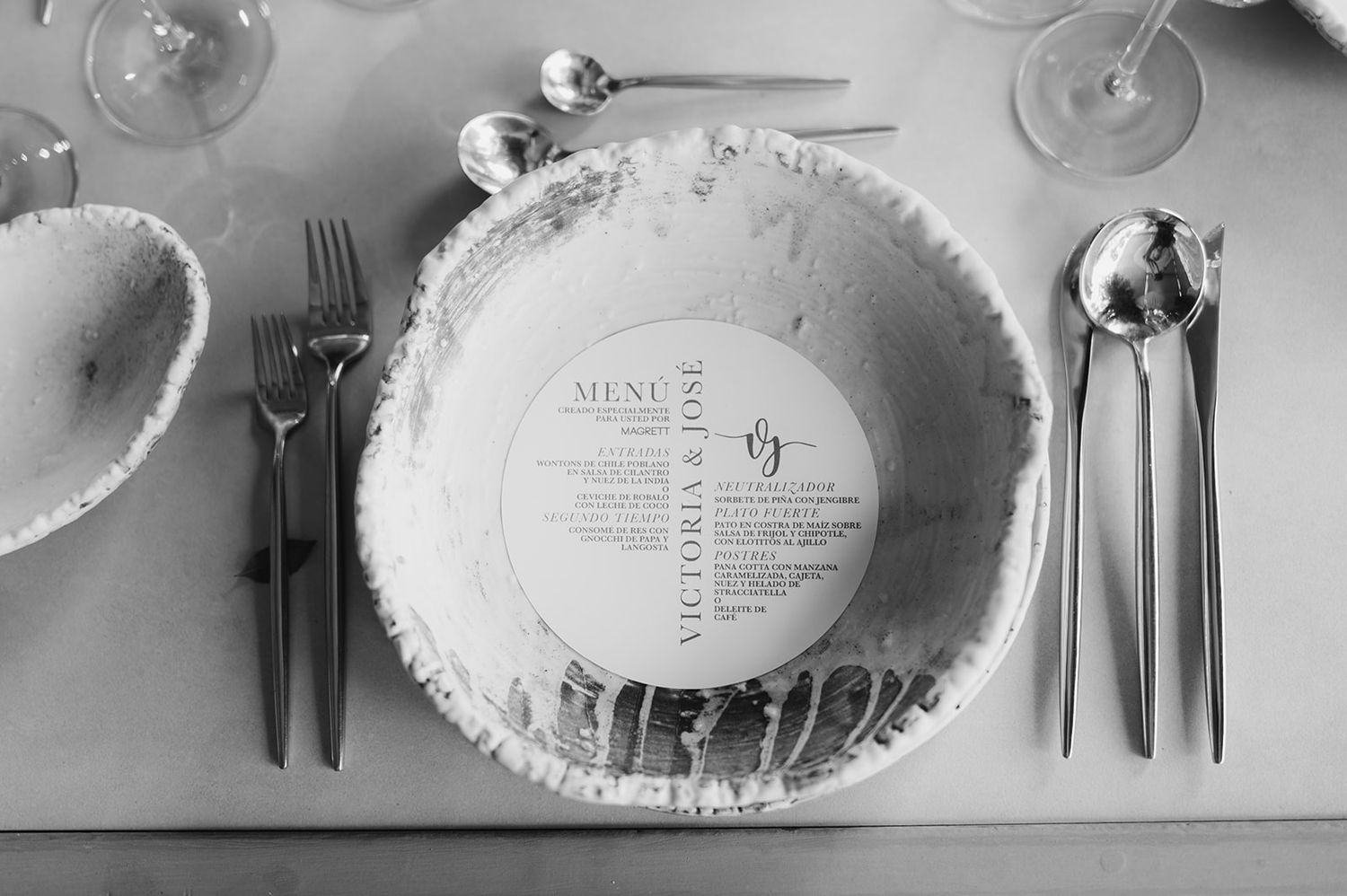 Elegant black and white wedding place setting with circular menu card in textured bowl flanked by silverware.