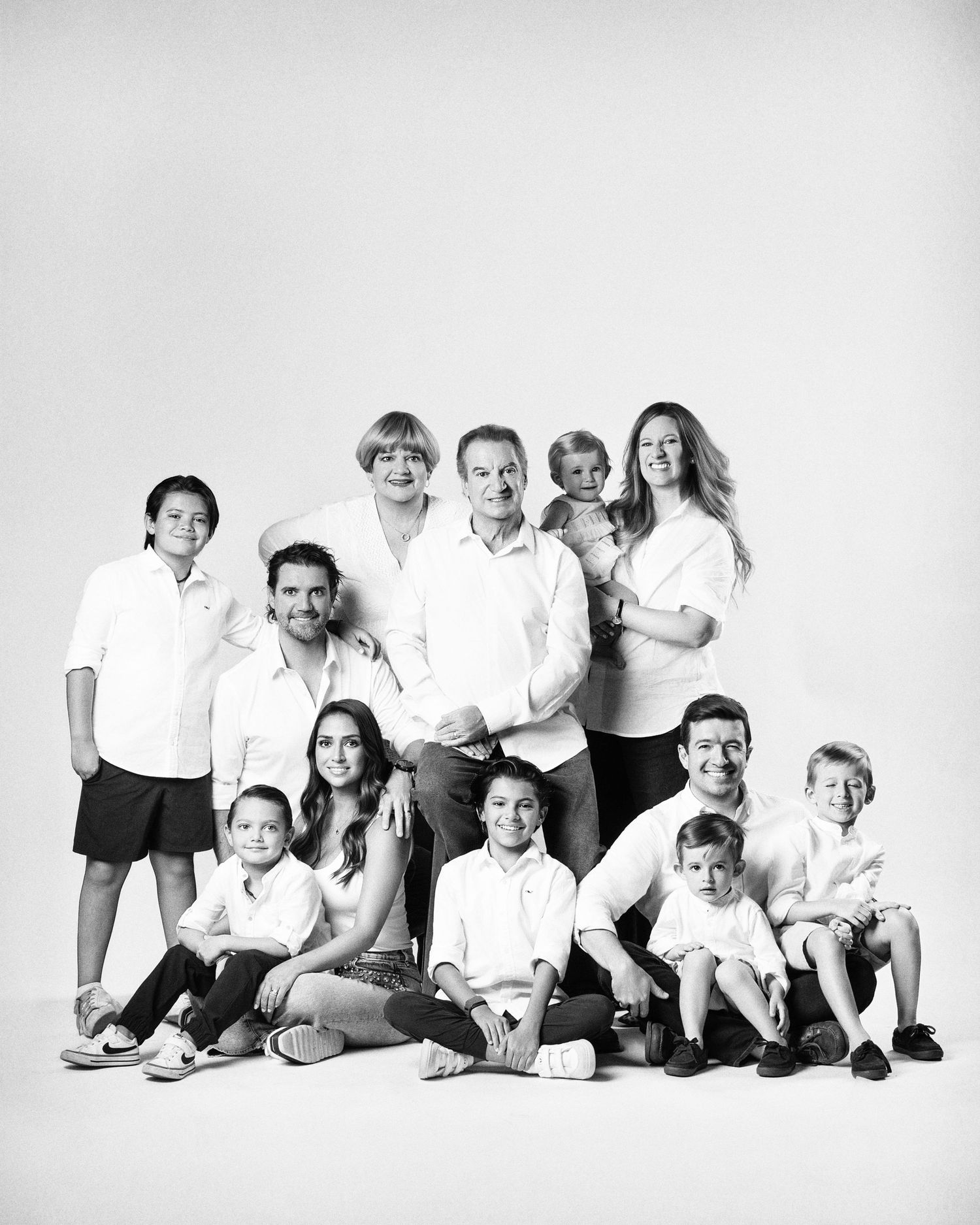 Black and white family portrait of multigenerational group in white shirts posing together in a studio setting.